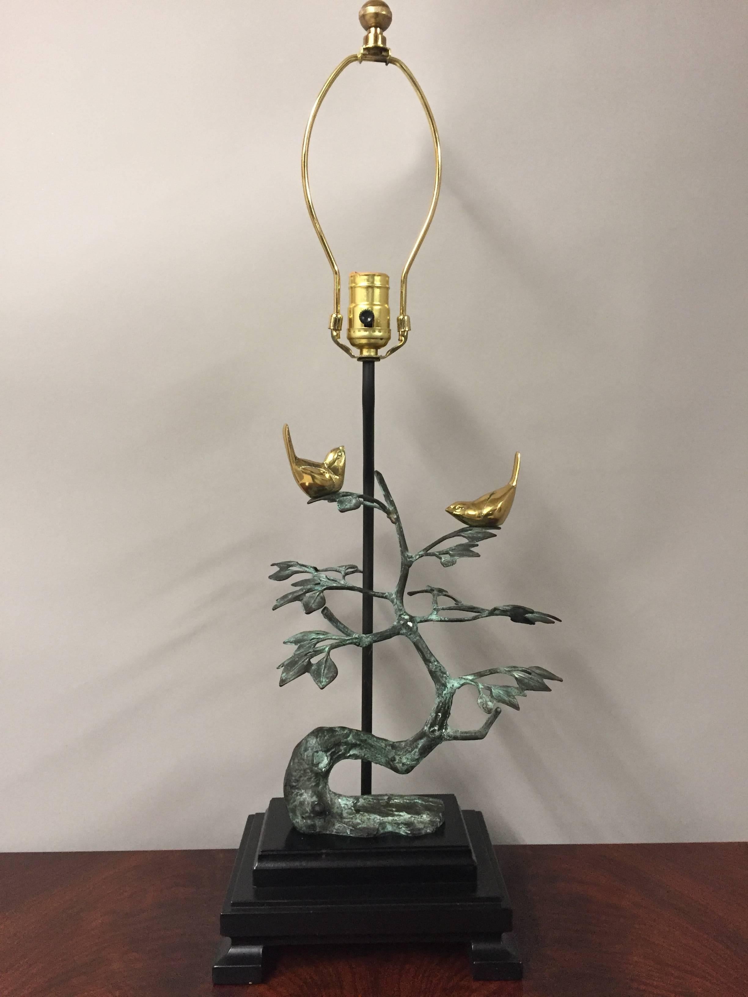 A lovely sculptural table lamp having a verdigris bronze stylized tree with two brass birds perched on the branches. Base is ebonized wood and shade is custom.