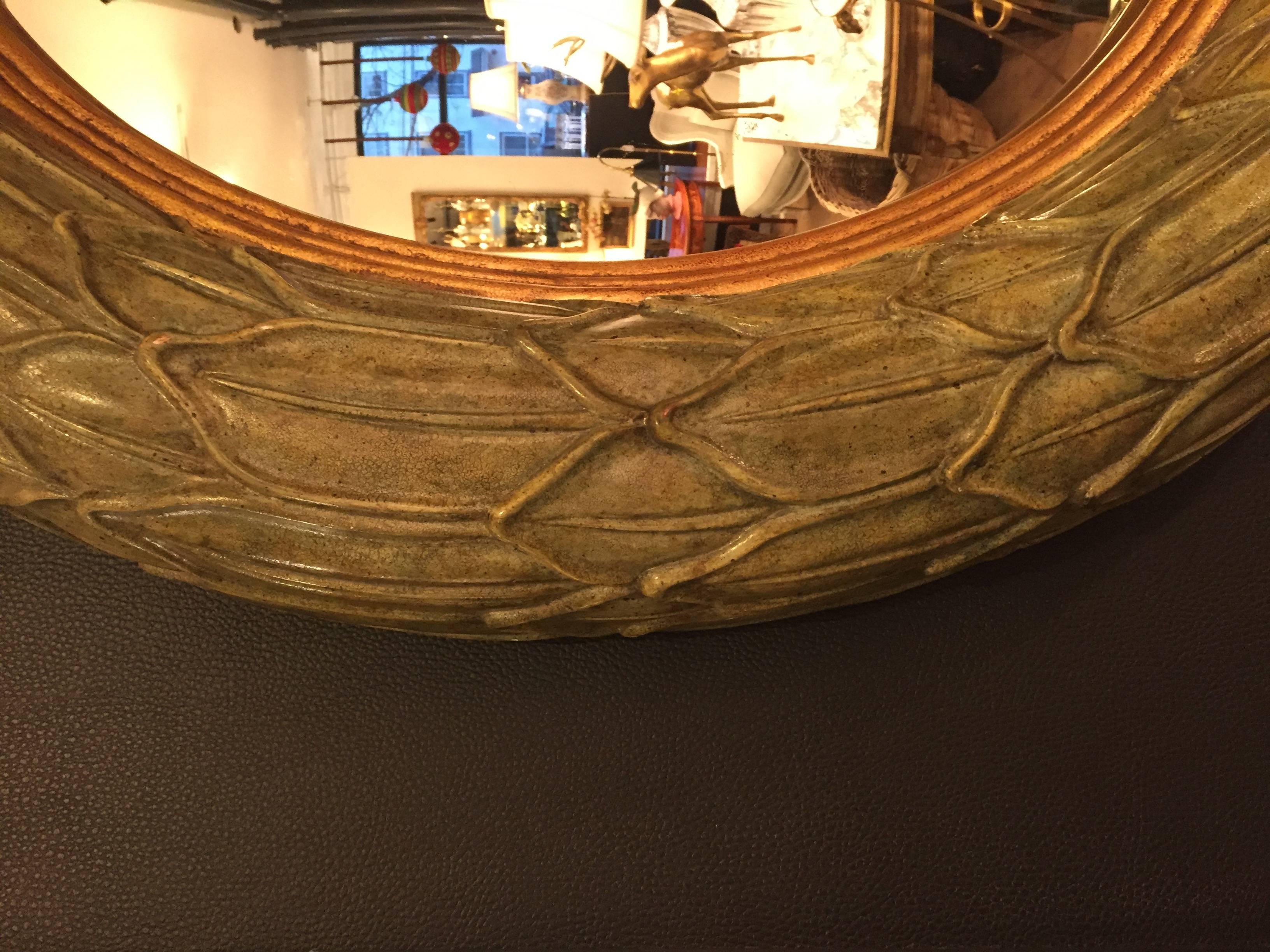 Chic round mirror having a light green painted carved wood frame with gold leaf detailing surrounded a convex shaped mirror.