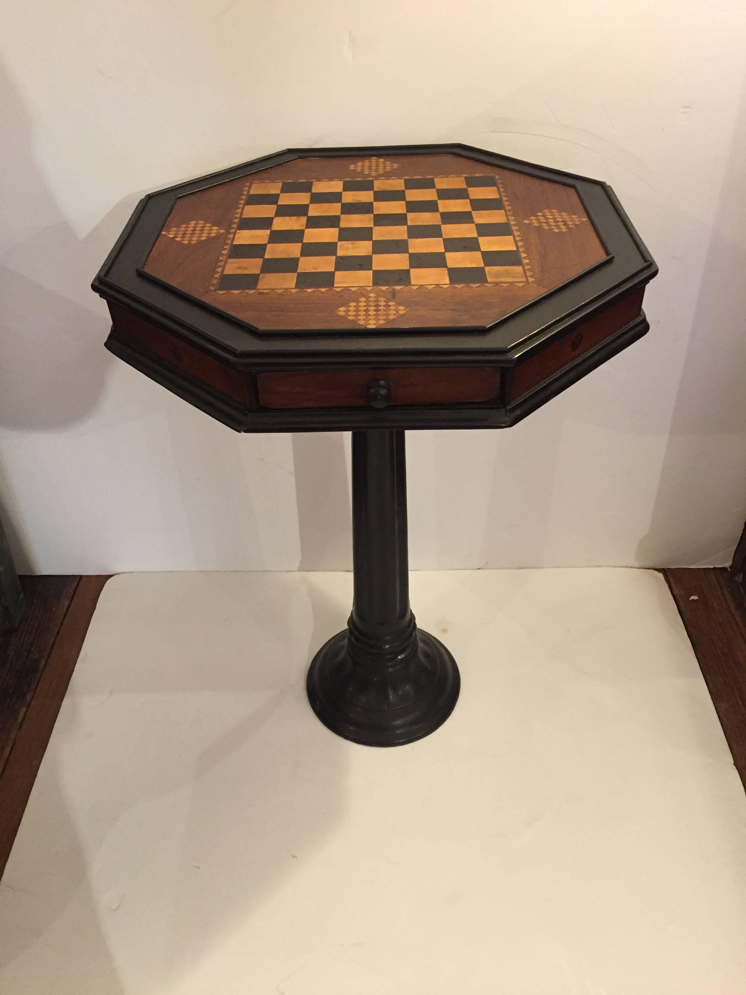 Great looking inlaid wood game or side table having a handsome octagonal top with decorative checkerboard in black and light brown against a rich brown background, all framed in ebonized wood. Base is a 9