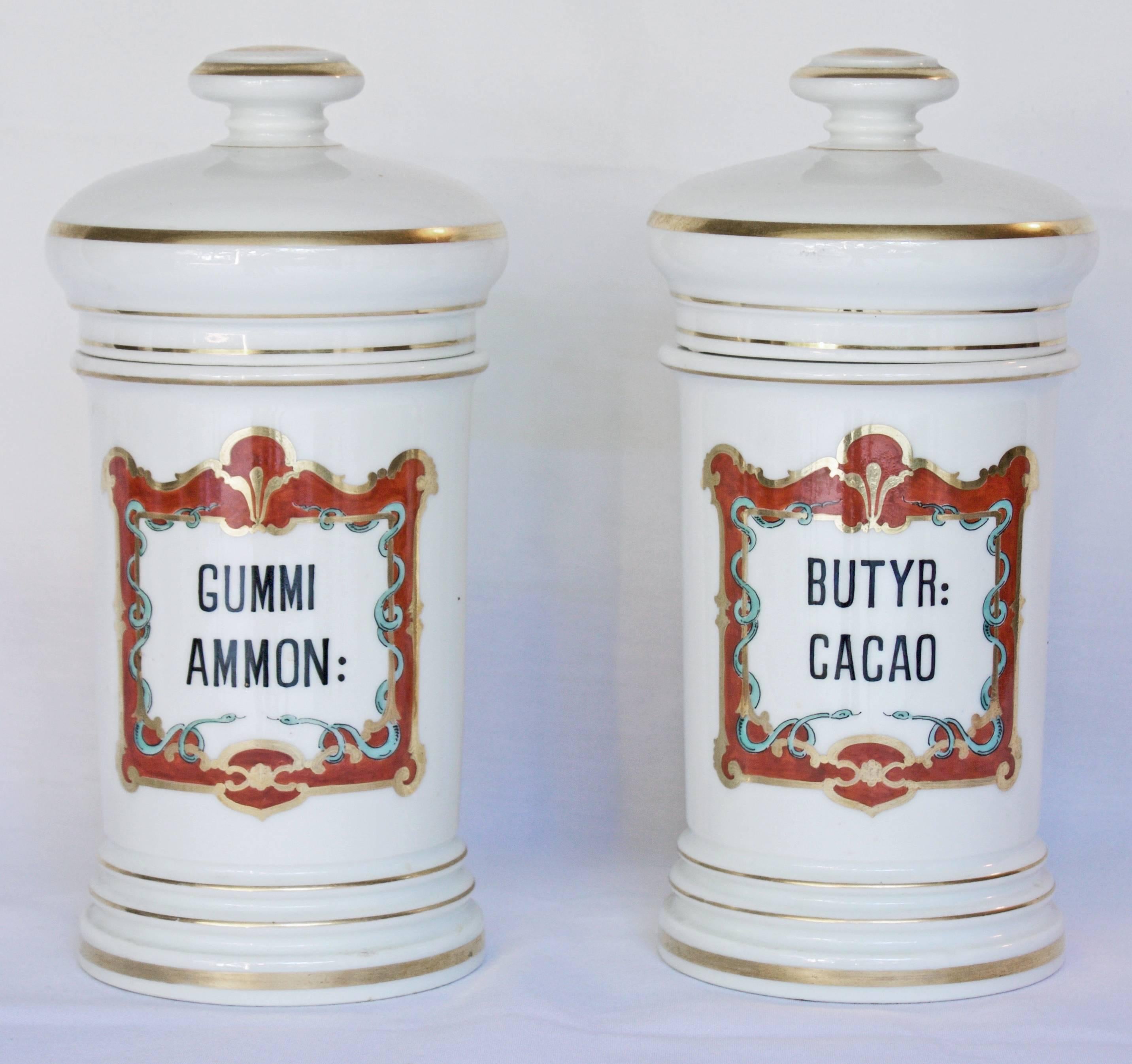 Handsome pair of white and solid porcelain jars each decorated with an hand-painted black label surrounded by a gorgeous reddish frame adorned with 24-karats gold and two blue snakes figures, the Medecin symbol. Gilded domed lid with a knop finial.