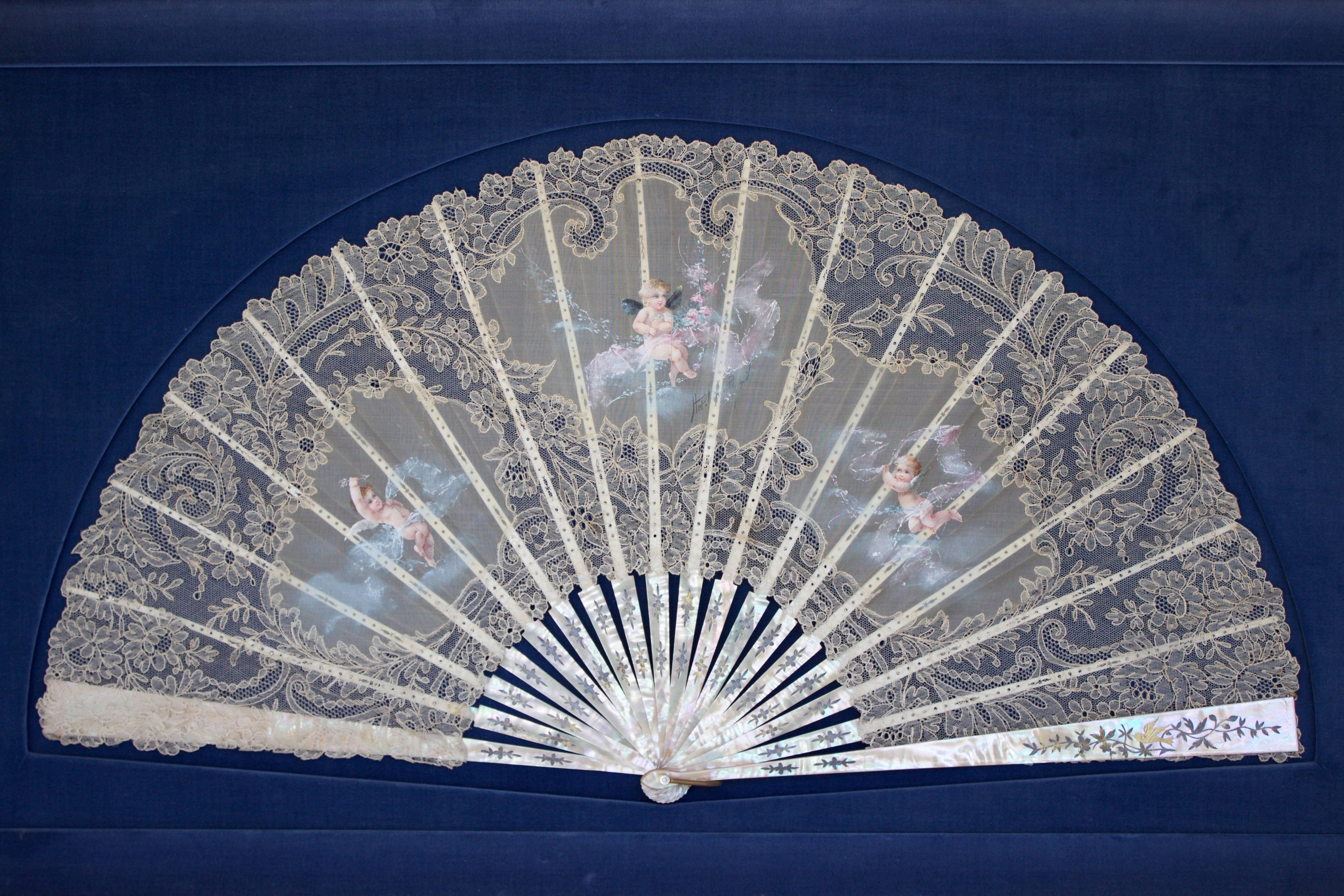 Beautiful hand fan with gorgeous 18 mother-of-pearl supports held together by a brass ring and covered by hand-painted putti on the lace. Mounted on a high quality fabric covered support and framed with a glass front.