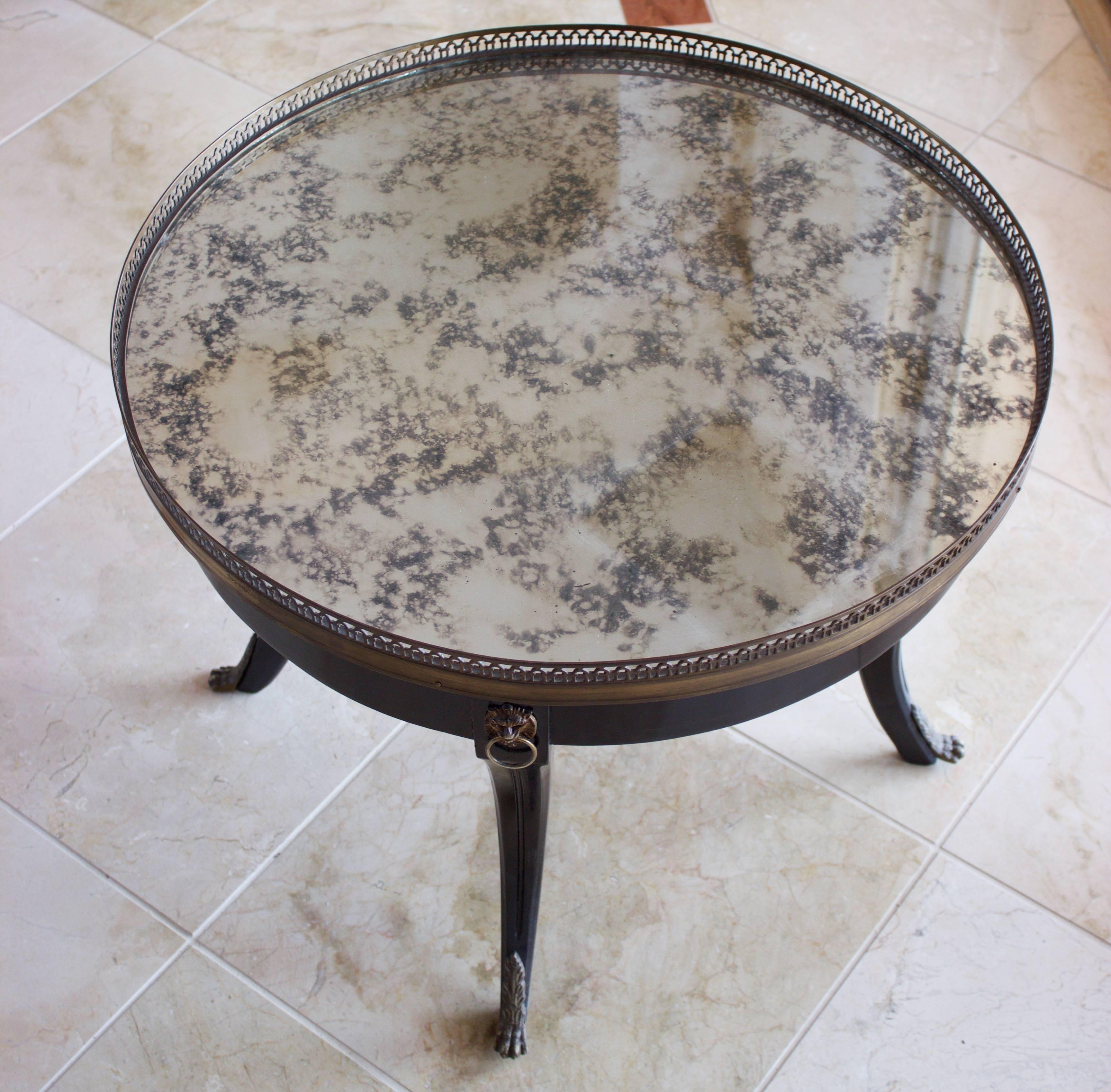 In Maison Jansen style, small round ebonized table with a gorgeous antique silvered mirror glass top surrounded by an openwork bronze gallery. Resting on four arched legs adorned each by a lion's head at top and Lion's foot at bottom.