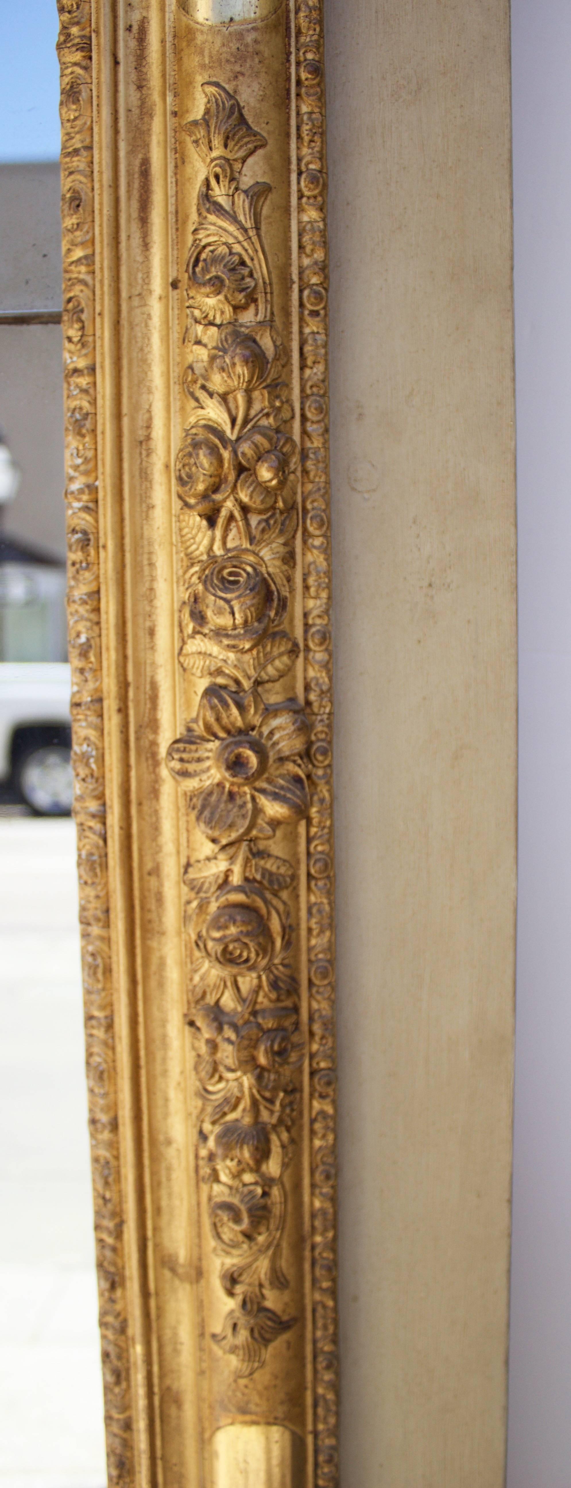 Gorgeous mirror frame adorned by in relief floral motifs in gilded carved wood and molded stucco. The entire trumeau in lacquered wood board with its top having a carved and gilded decor of a central flowers basket surrounded by a garland, flying
