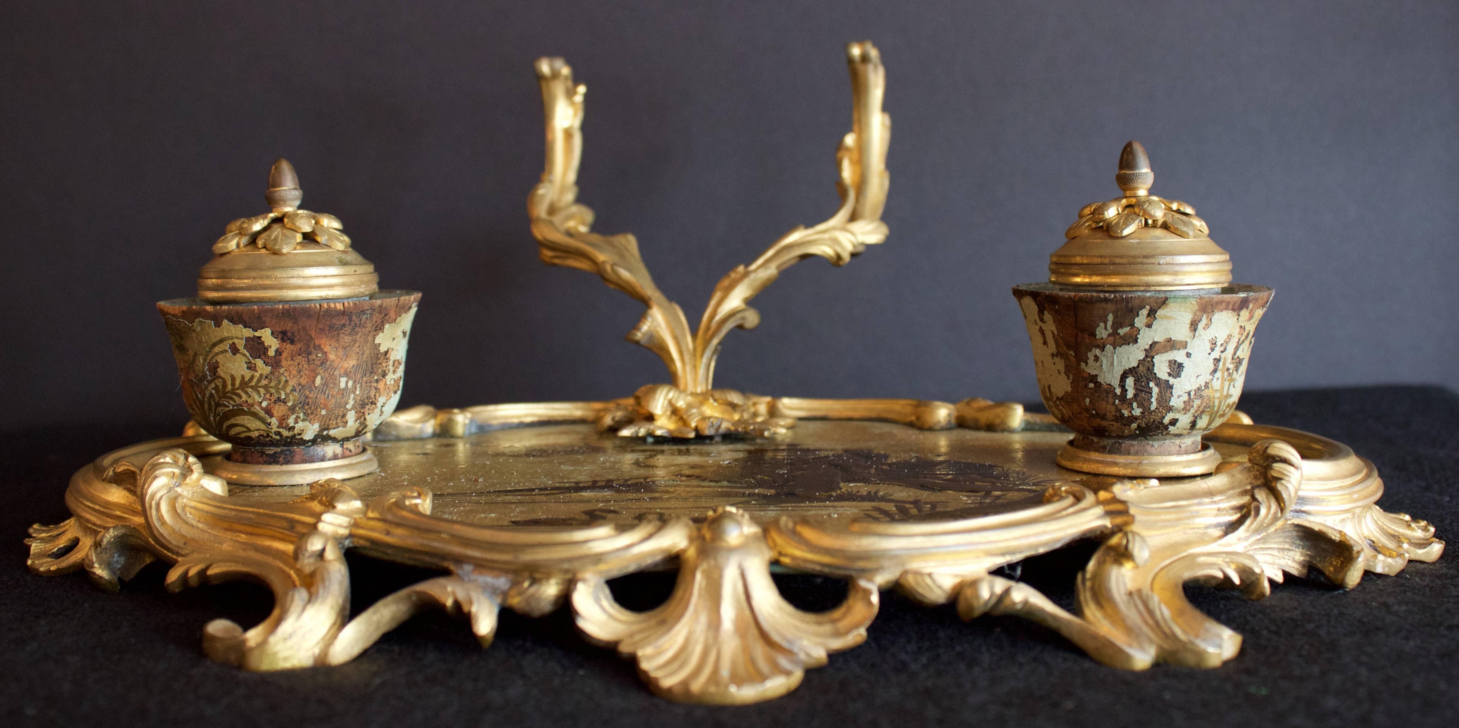 Rare and superb Louis XV period inkstand finely chased and gilded bronze base in a Rocaille decor of stylized leaves and shells. At top, resting on a Chinoiderie lacquered wooden tray the Rocaille gilt bronze pen holder and two inkwell in gilt