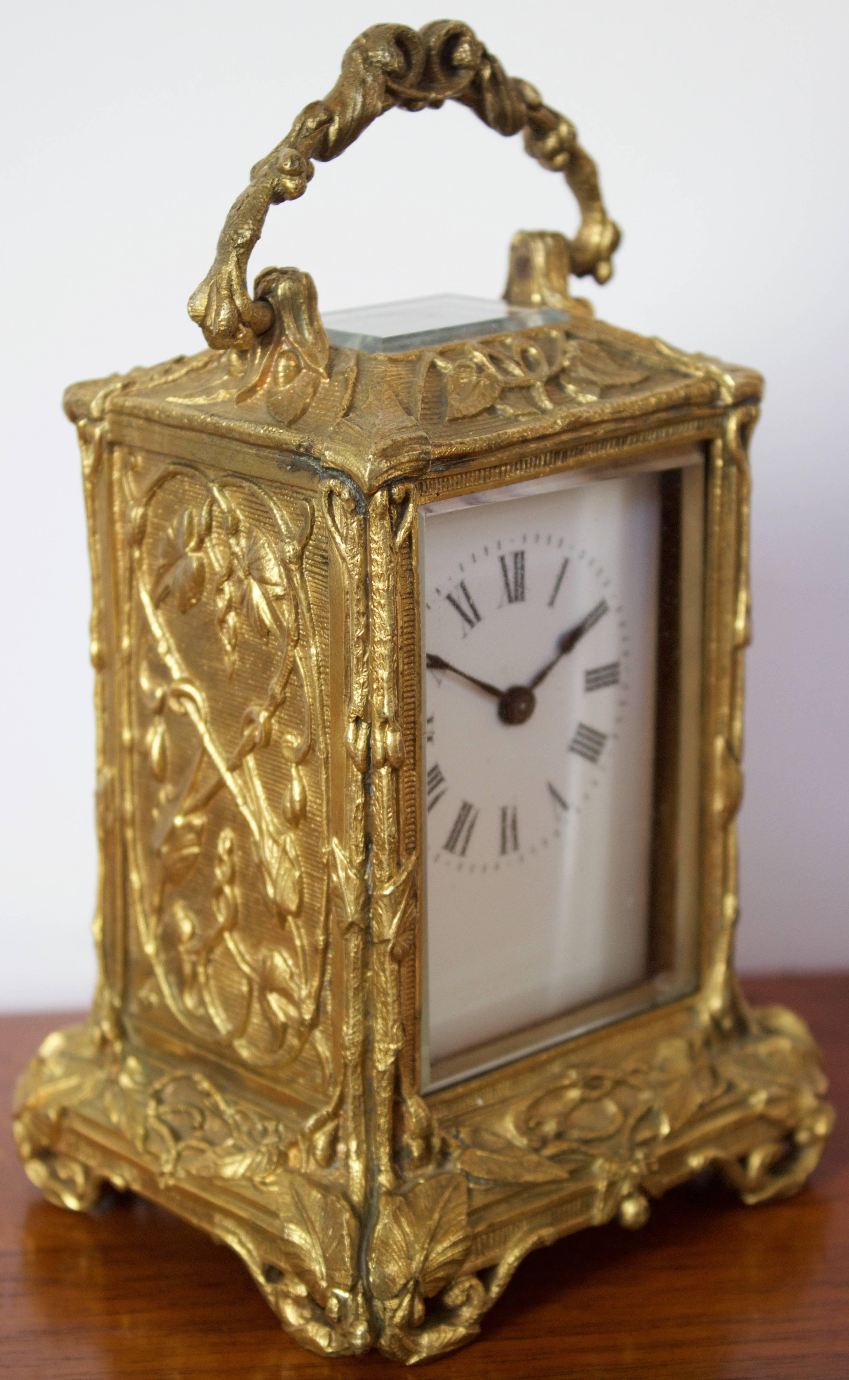 A lovely French carriage clock in a bronze dore case finely decorated with a scrolling vine decor, pierced bracket floral form feet and surmounted by a hinged loop handle. Enameled dial with Roman numerals and beveled glass panel in front and on