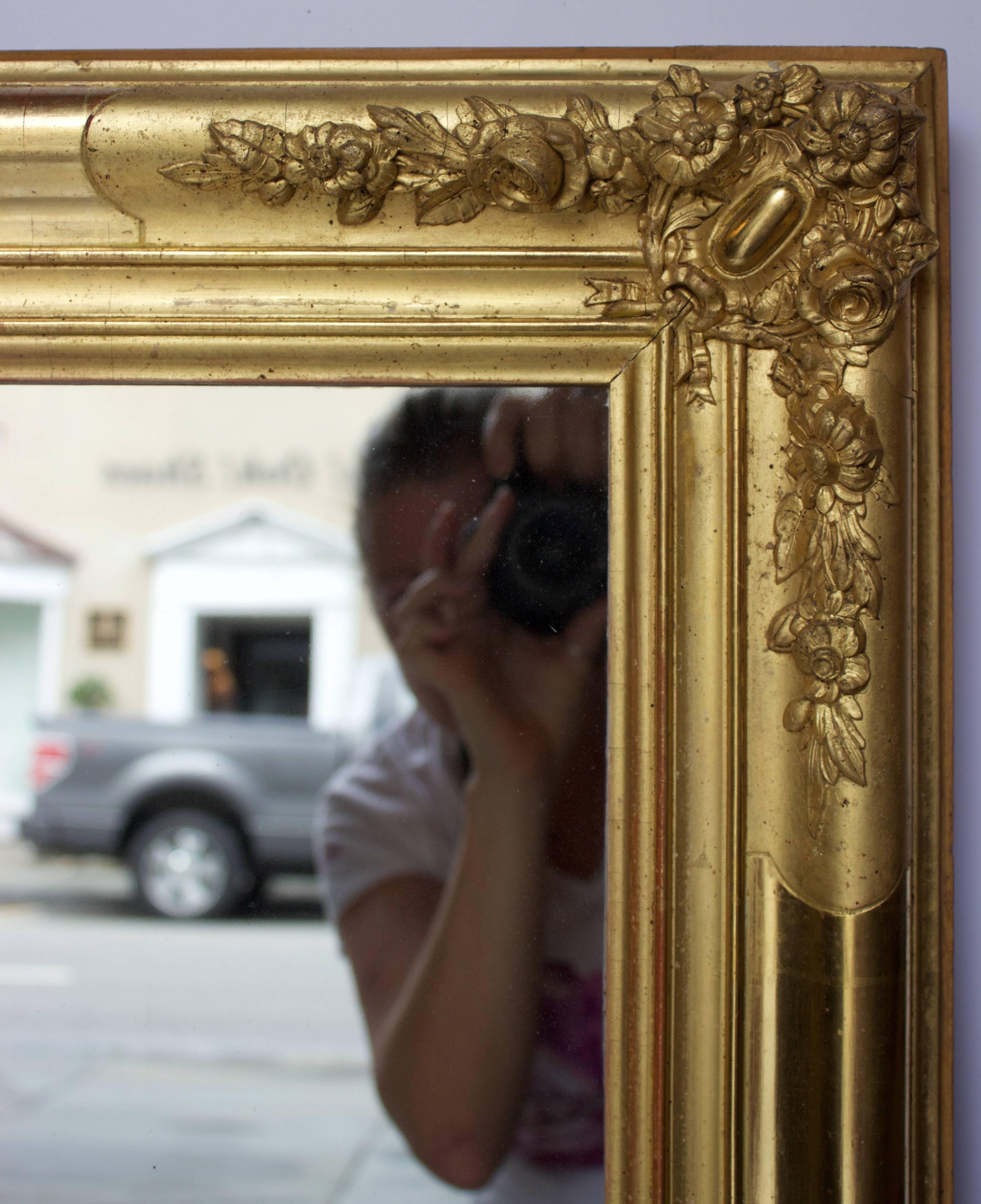 This gorgeous mirror reflects perfectly what a French Restauration (1815-1830) period mirror should be: Wooden frame with water gold gilt decor alnernatively high and low sheen and ornated by gesso molded and gilded flowers on all four