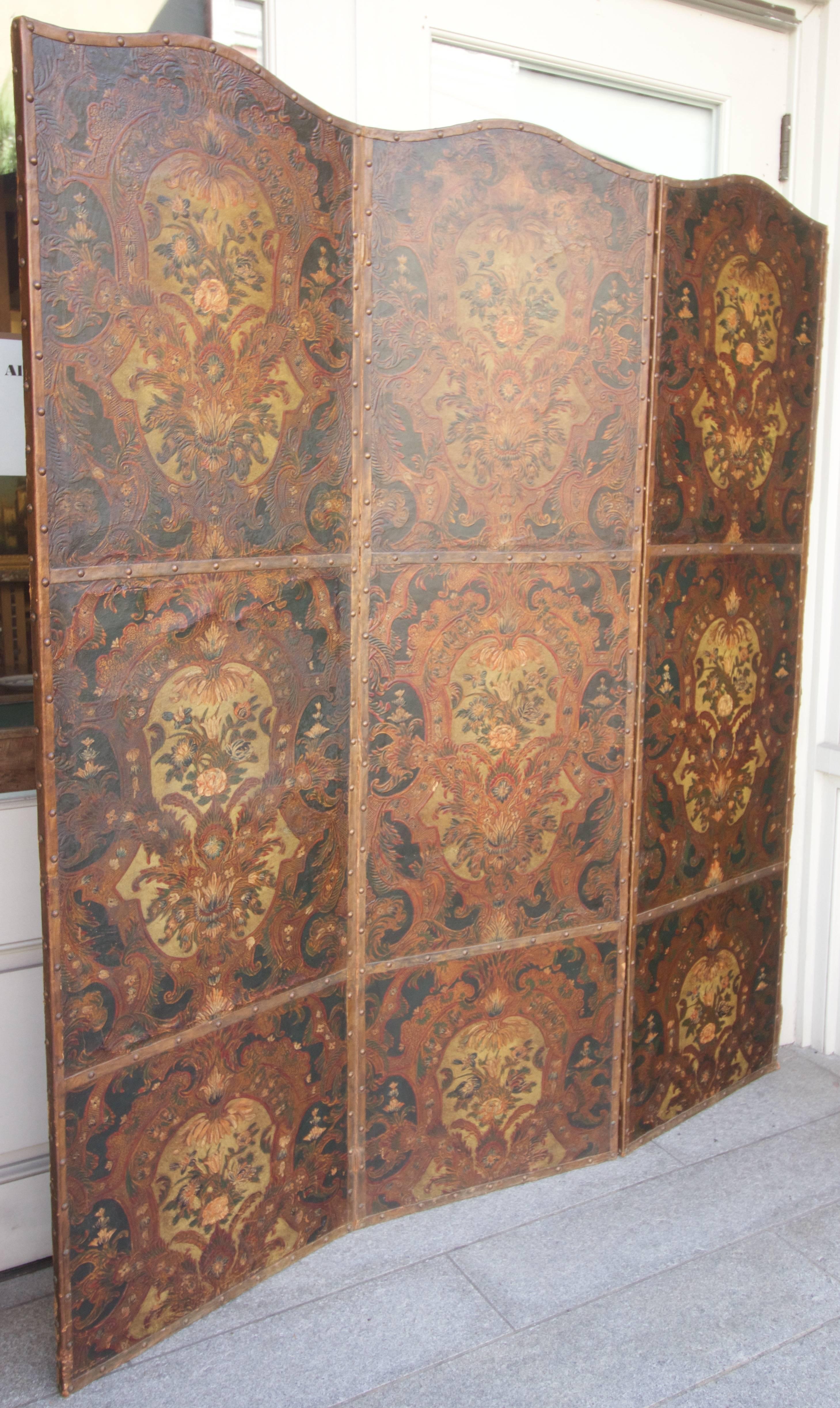 An antique screen wonderfully embossed, painted and gold leafed leather panels slightly 