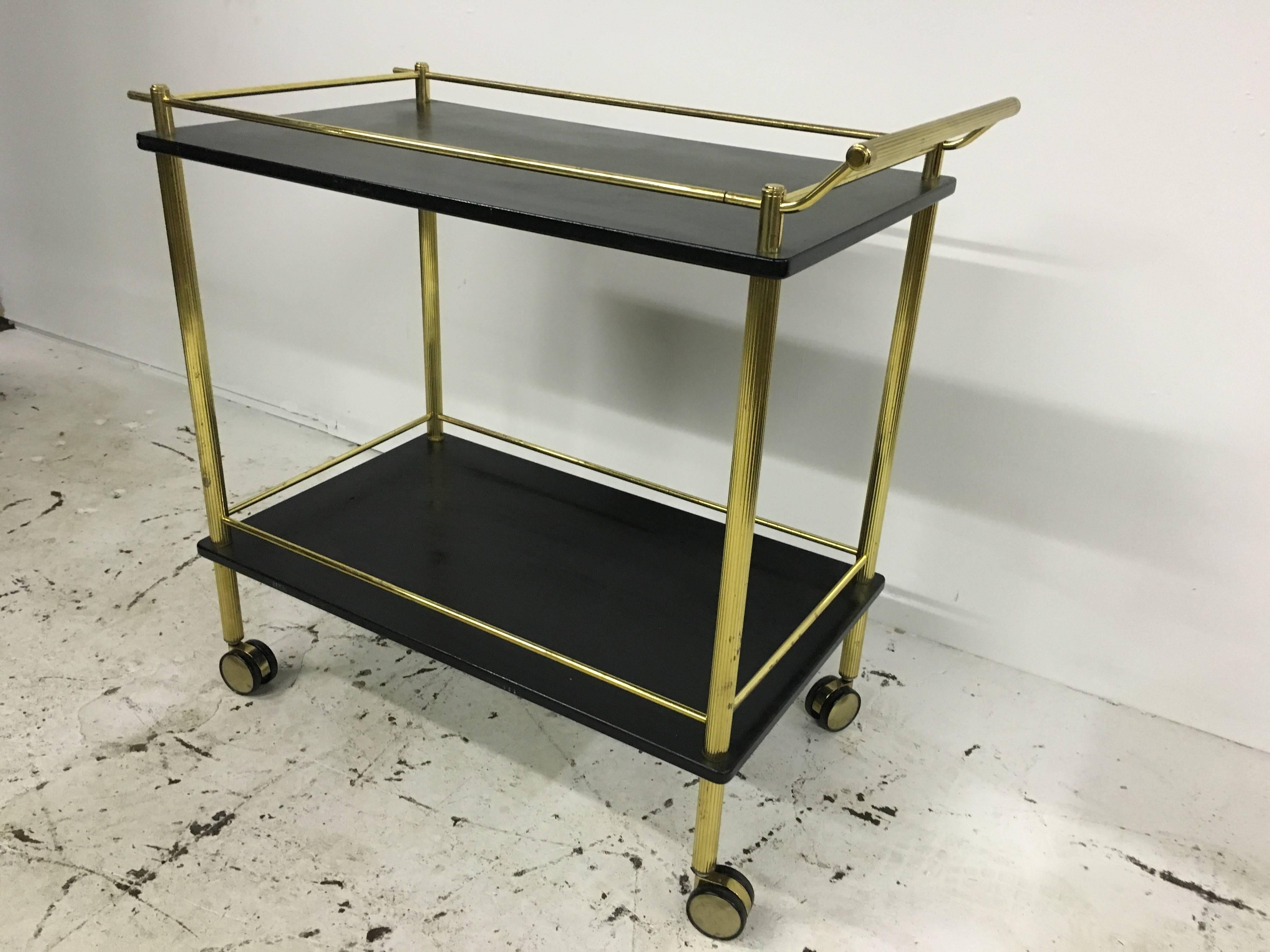 1970s bar cart, of sleek design with rectangular two tiers of black lacquered shelves with conforming brass handles and gallery raised on four castors.