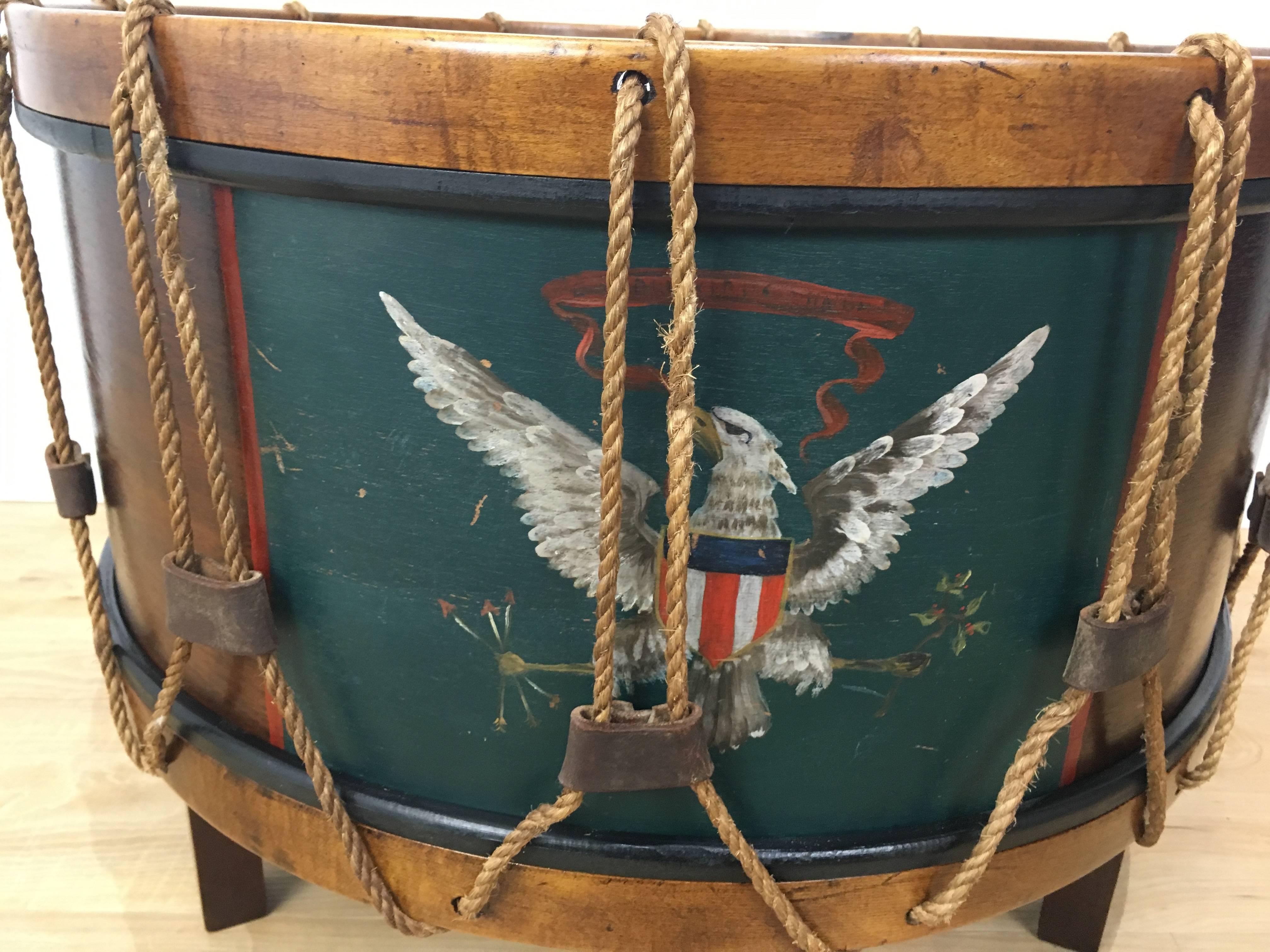 United States Military drum cocktail table, realistically modeled as a Military drum, with inst black glass top, the body painted with Presidential seal and continuous rope over the sheave of the drum, raised on tapering square legs.