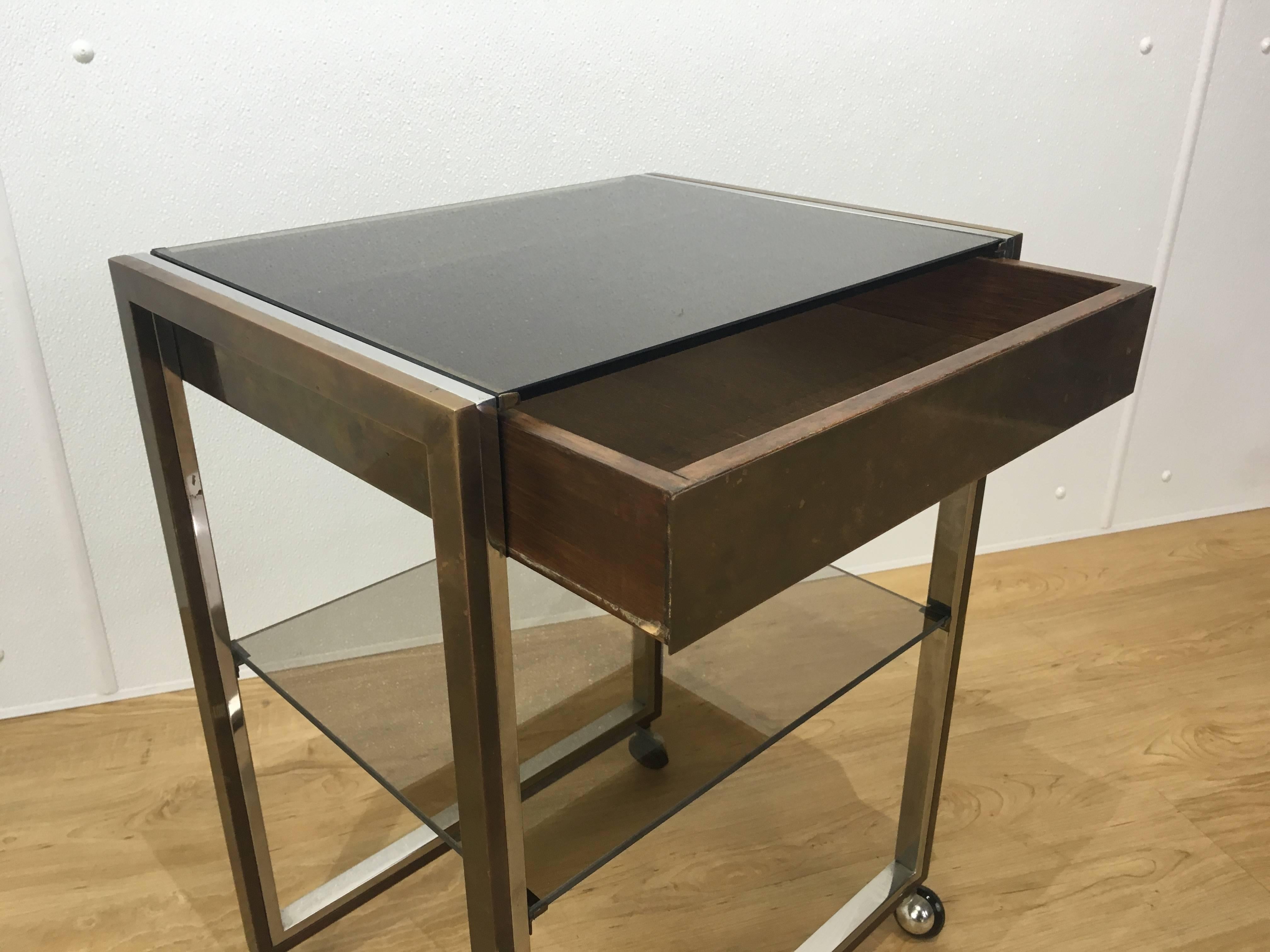 Mastercraft side table, of diminutive form with bronze glass top fitted with one drawer and middle bronze glass shelf. Supported by two-tone well cast metal frame raised on four castors. Great for living room, bedroom or office.