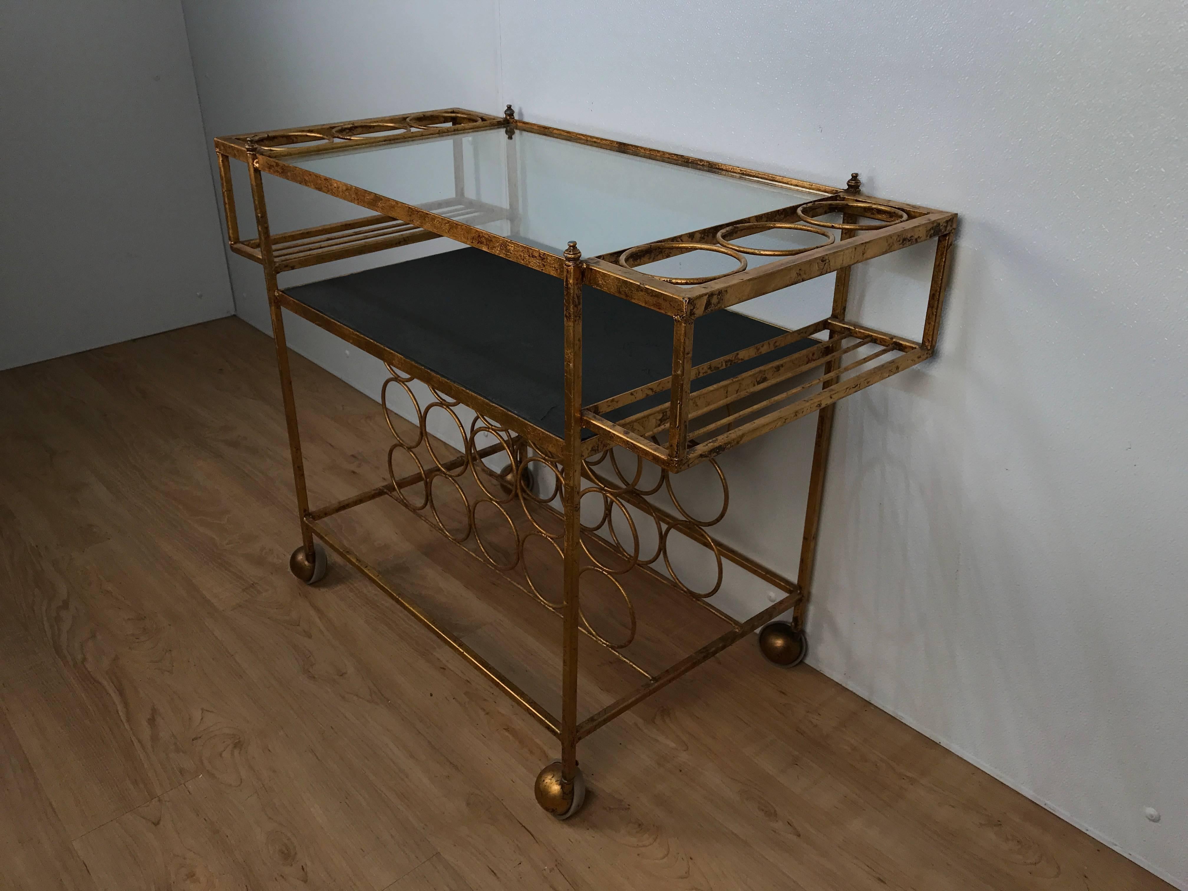 1970s, gilt acid washed bar cart, form and function perfection the top with inset glass top flanked by six bottle caddy. The lower shelf of inset slate, the bottom rack holds 15 bottles.
          