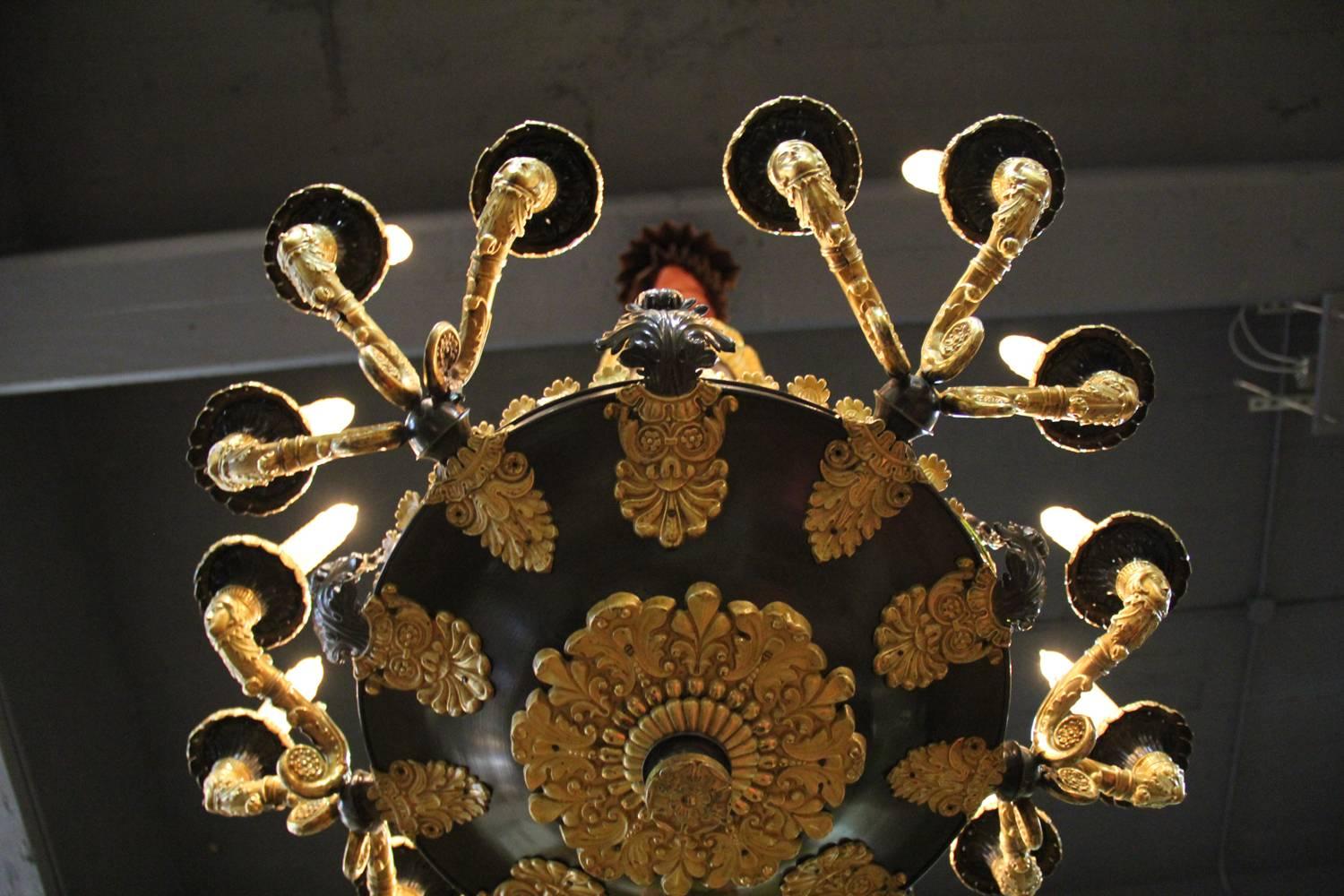 A 19th century gilt bronze French Charles X fifteen-light chandelier, with a carved canopy above a tent of five suspending "cables" and supporting the fifteen masked and scrolling candle arms emerging from the bronze bowl, accented with