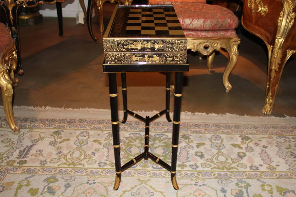 A 19th century English import chinoiserie black lacquer games or cocktail table with later gate leg stand, that when closed creates a 11 3/4" deep profile, the foldable game board with chinoiserie detailing throughout, the board has one side