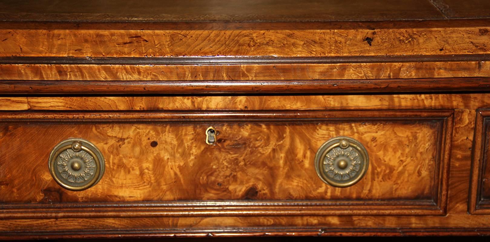 A 19th century English Regency burl elmwood and parcel-gilt partners desk, the later C. Mariani leather writing surface embossed above six drawers (three on each side) and raised on splayed legs terminating on brass caster feet connected by a turned