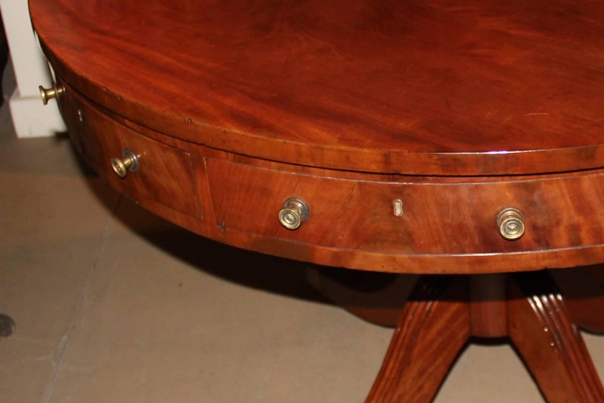 A 19th century English mahogany drum table, with four drawers and four faux drawers, and raised on a Sheraton pedestal base with four outflaring legs terminating in brass casters.