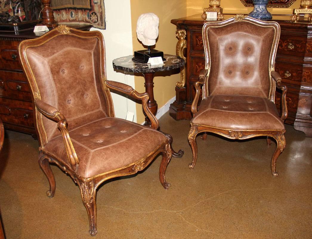 A pair of 18th century Italian Louis XV walnut and parcel-gilt armchairs with later C. Mariani custom antiqued leather seats and backs, accented with stitching and conforming leather rosettes, the arms embellished with nailhead trim and the frame