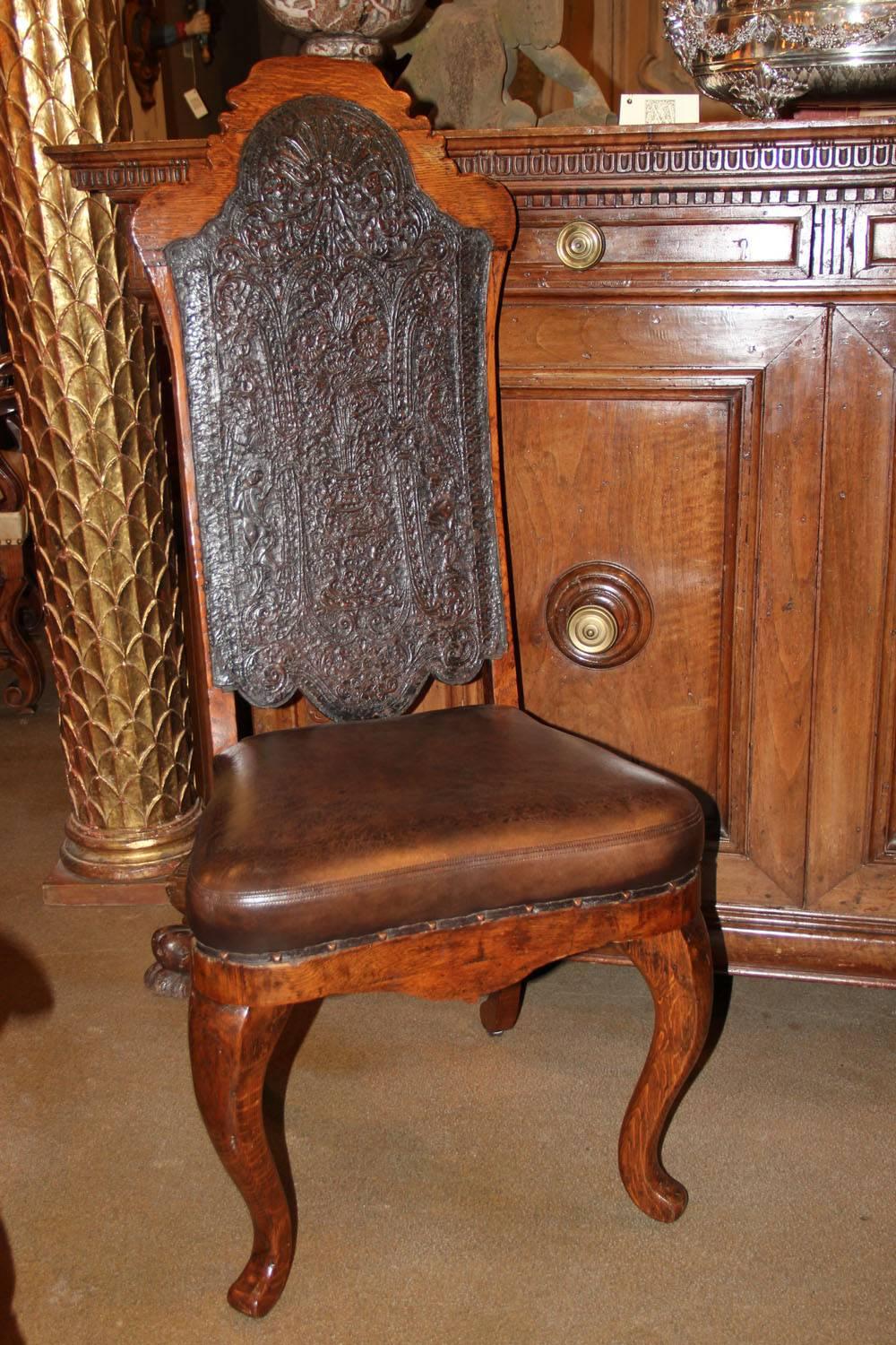 An 18th century Portuguese oak chair, the original leather-embossed inset back depicting flowers in an urn surrounded by foliate and floral motifs, the later antiqued leather seat accented with nailhead trimming, the whole raised on two cabriole