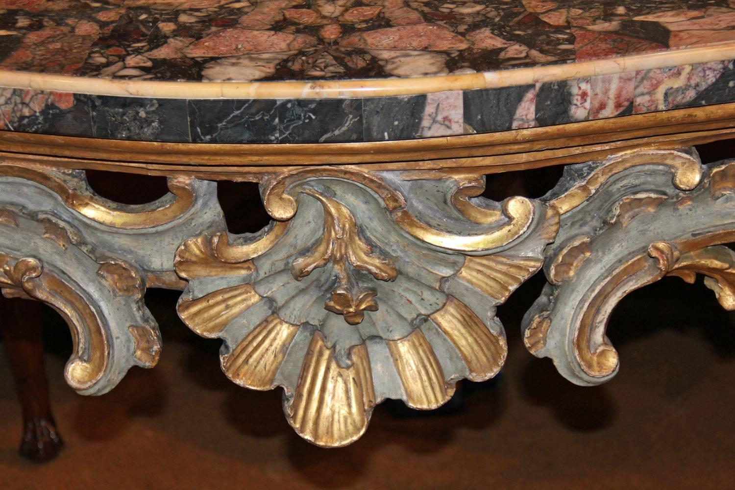 An 18th century Venetian pale blue polychrome and parcel-gilt console retaining its original marble top in hues of pink, red, gray, and white and with a Siena marble edge, above a carved apron centered by scallop shell and rocaille motifs, the four