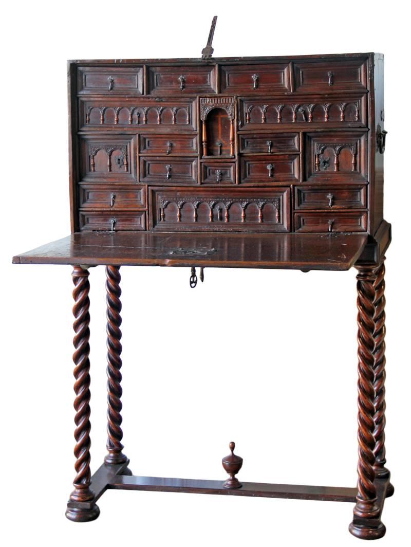 A 16th century Spanish walnut and leather Vargueño on a later stand, the rectangular chest retaining its original iron handles, lock and key, the fall front with iron and leather appliqués and opening to reveal a fitted interior with 19 drawers and