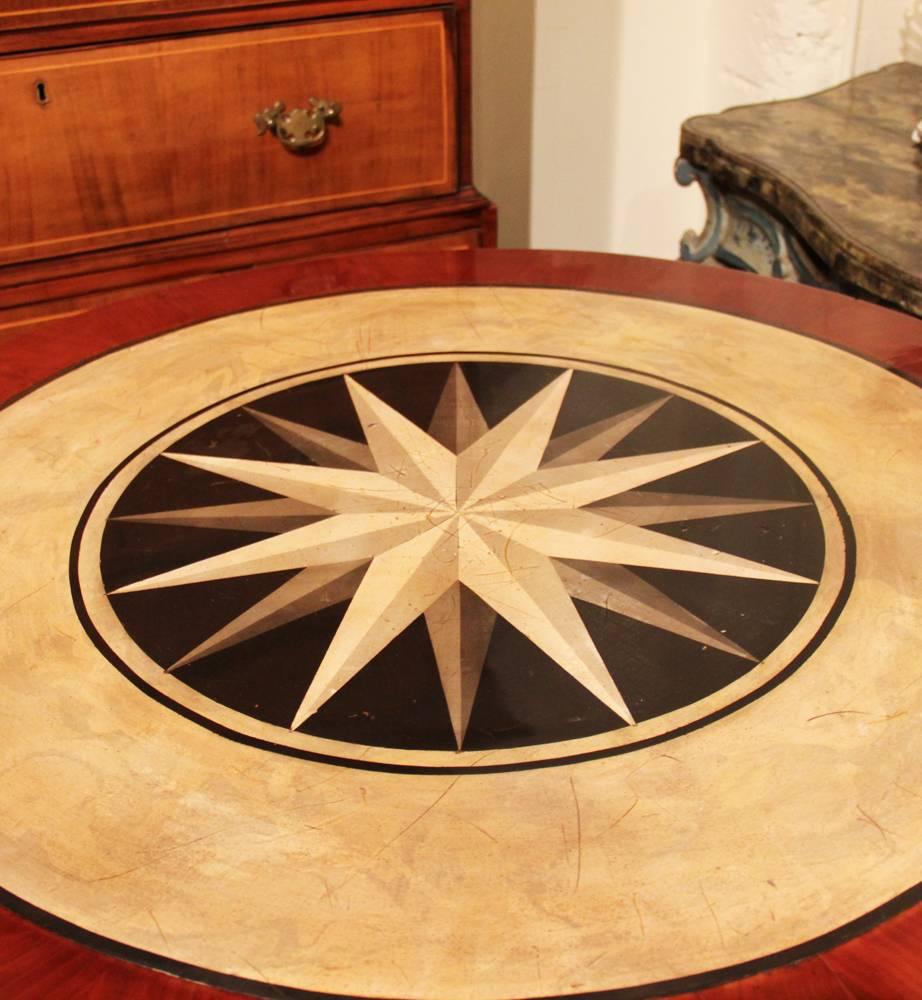 A 19th century Italian mahogany, parcel-gilt and scagliola center table, the scagliola top and base embellished with differing stellate patterns, with the whole raised on four columnar legs accented with gilded capitals and bases and all raised on a
