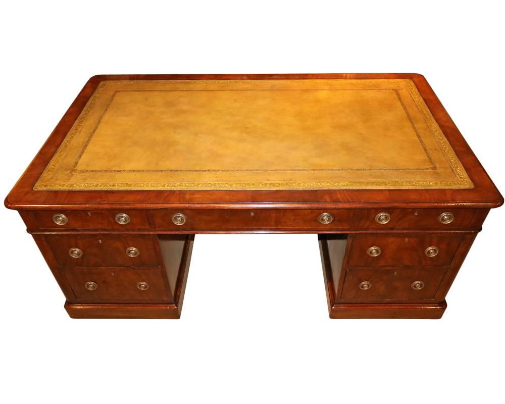 An English Regency mahogany partners' desk with multiple drawers and cabinets below an embossed leather writing surface and raised on a molded plinth.