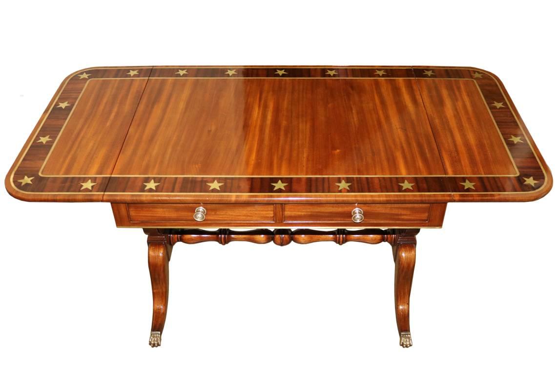 A 19th century English Regency mahogany sofa table, the top with a rosewood and brass stellate inlay border, above two drop leaves on either side, an apron fitted with two functioning drawers and two faux drawers on the reverse, raised on lyre legs