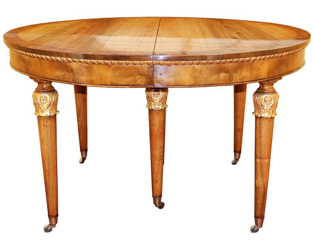 An 18th century, Italian parcel-gilt walnut expanding dining table with five 20-inch leaves (pictured with four), the top with a burl walnut border, the apron with gilded gadrooning, and the whole raised on five turned tapering legs accented with