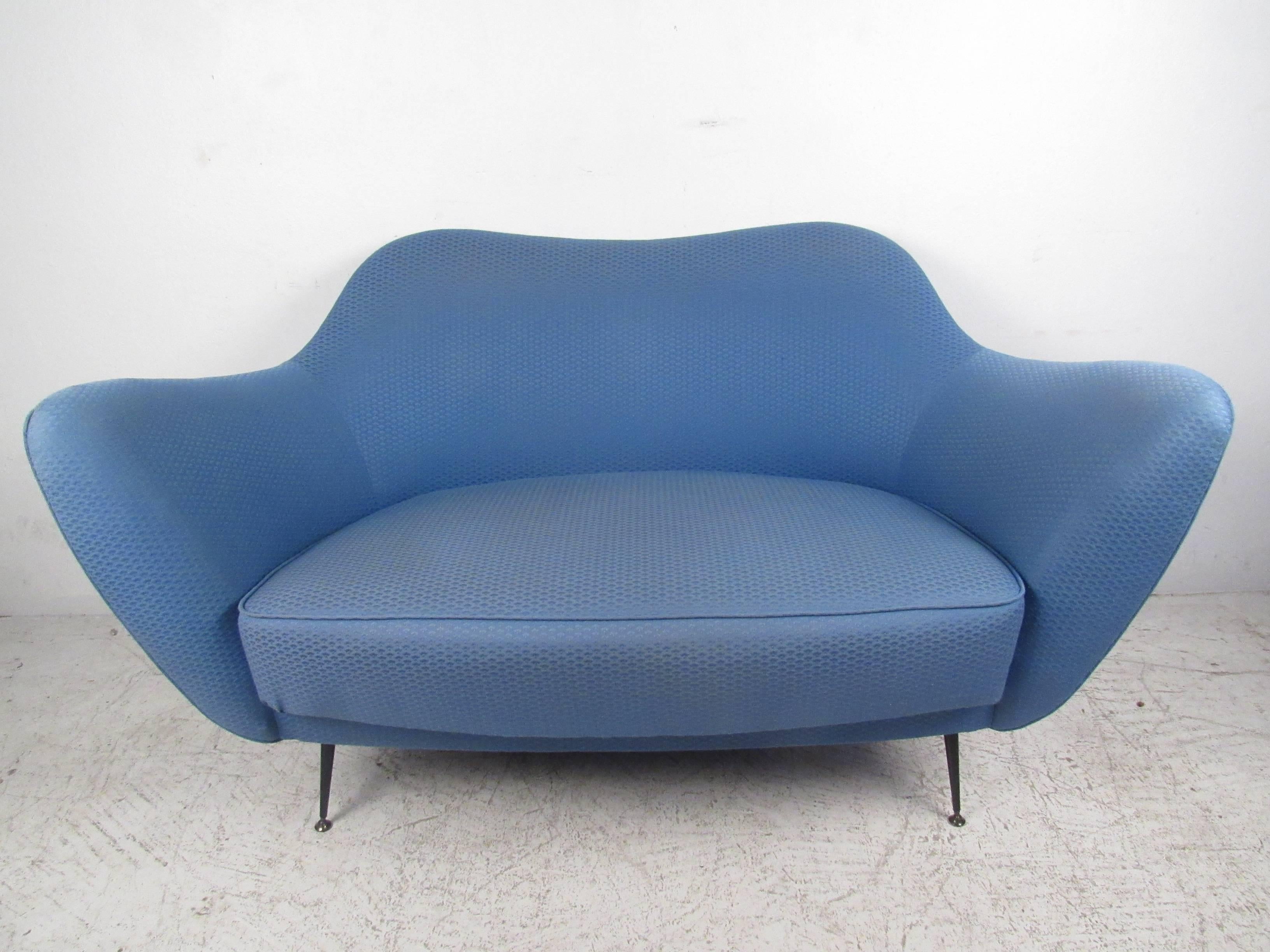 This unique midcentury loveseat features a beautiful sculpted back, tapered brass trim legs, and lovely vintage fabric. This comfortable and stylish two-seater is ideal for a variety of interiors. Pair of matching lounge chairs available, please