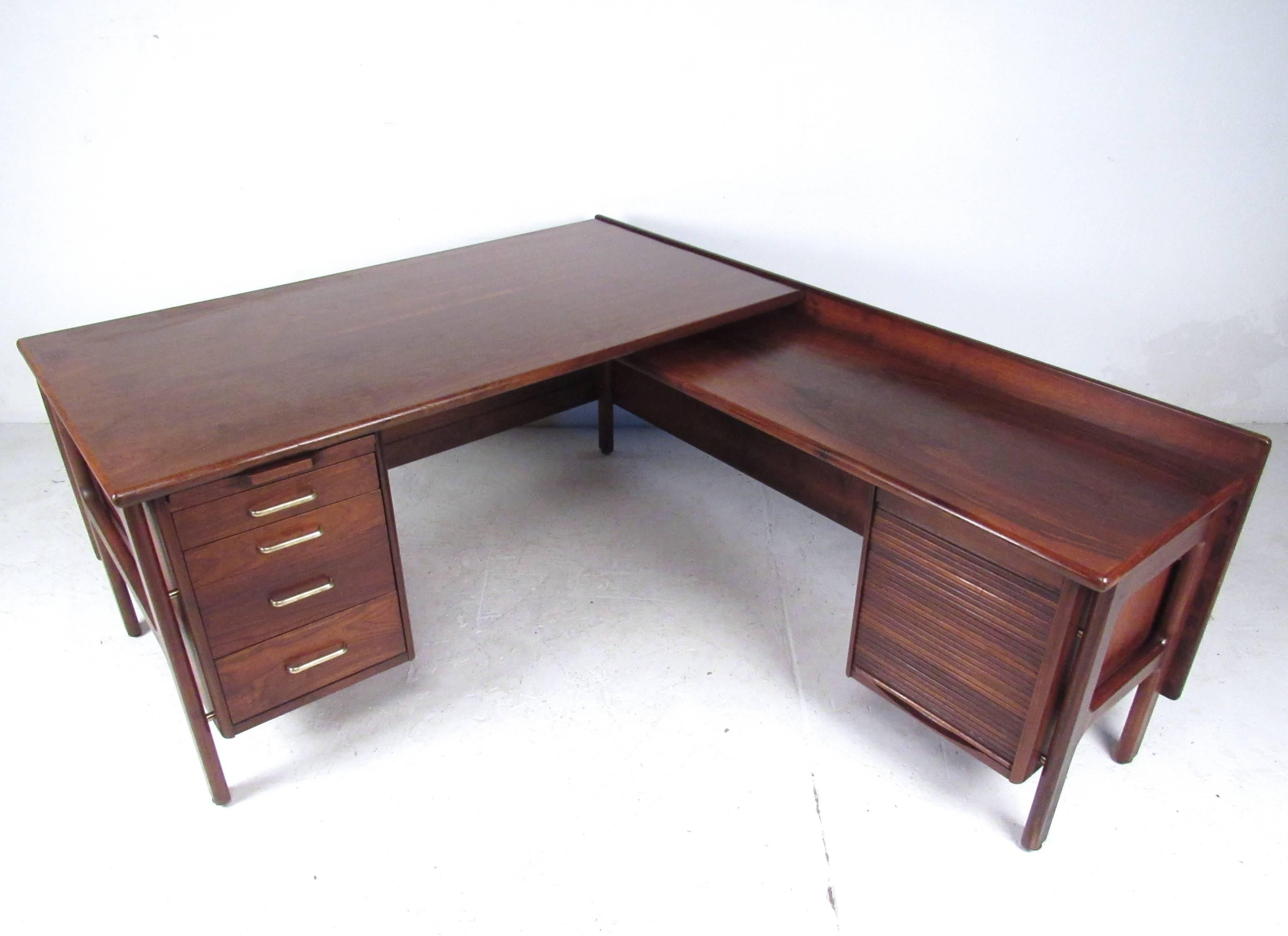This stunning vintage desk boasts a spacious two-tier L-shaped work surface, offering plenty of room for multiple computers, printers, or other office needs. Added storage in metal glide drawers and extra filing behind vertical tambour panel add to