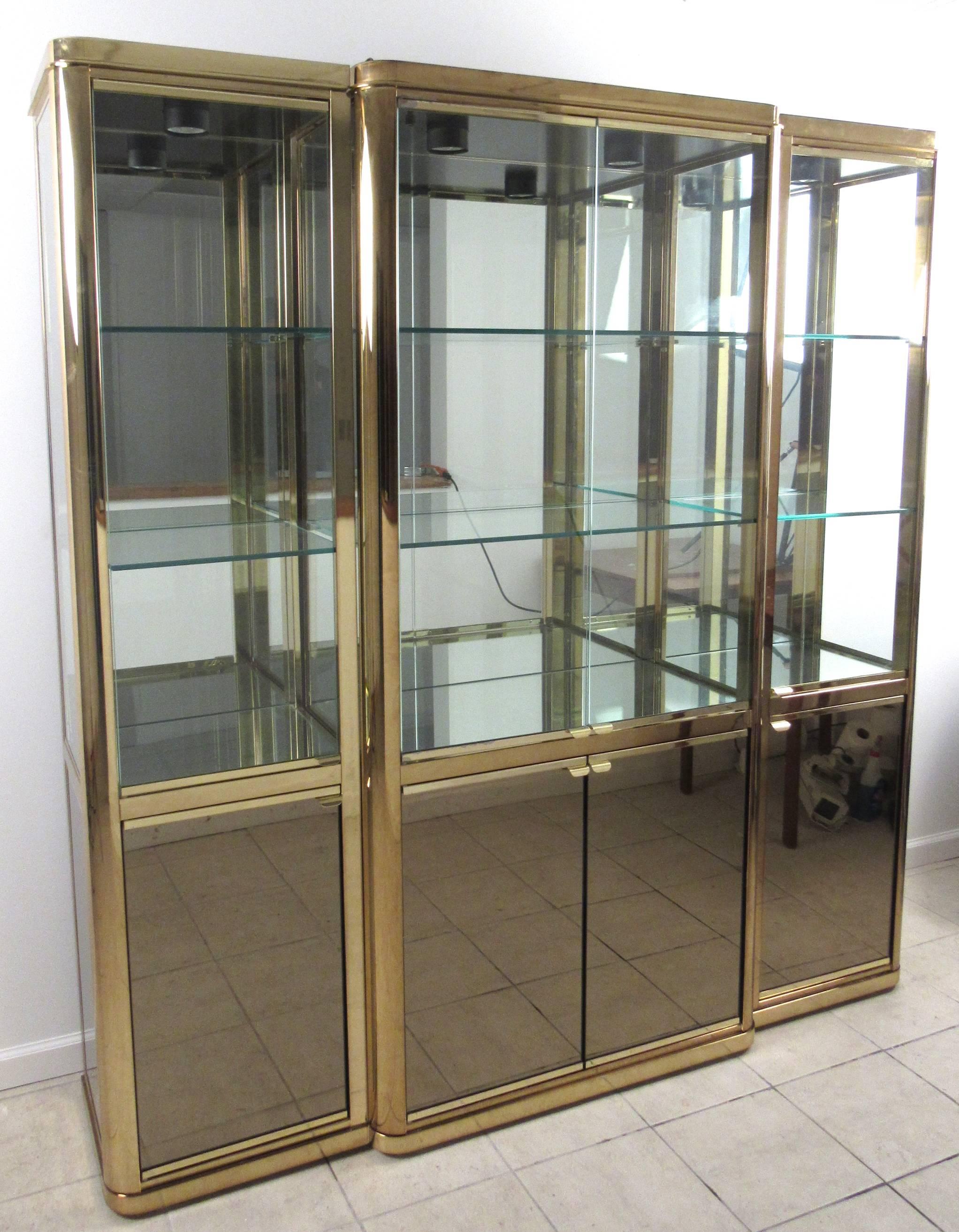 This unique three-piece brass and glass display case features wonderful smoked mirror cabinets topped with spacious glass display. Perfect piece for home or shop display, this top lit piece by Design Institute of America is a truly elegant vintage