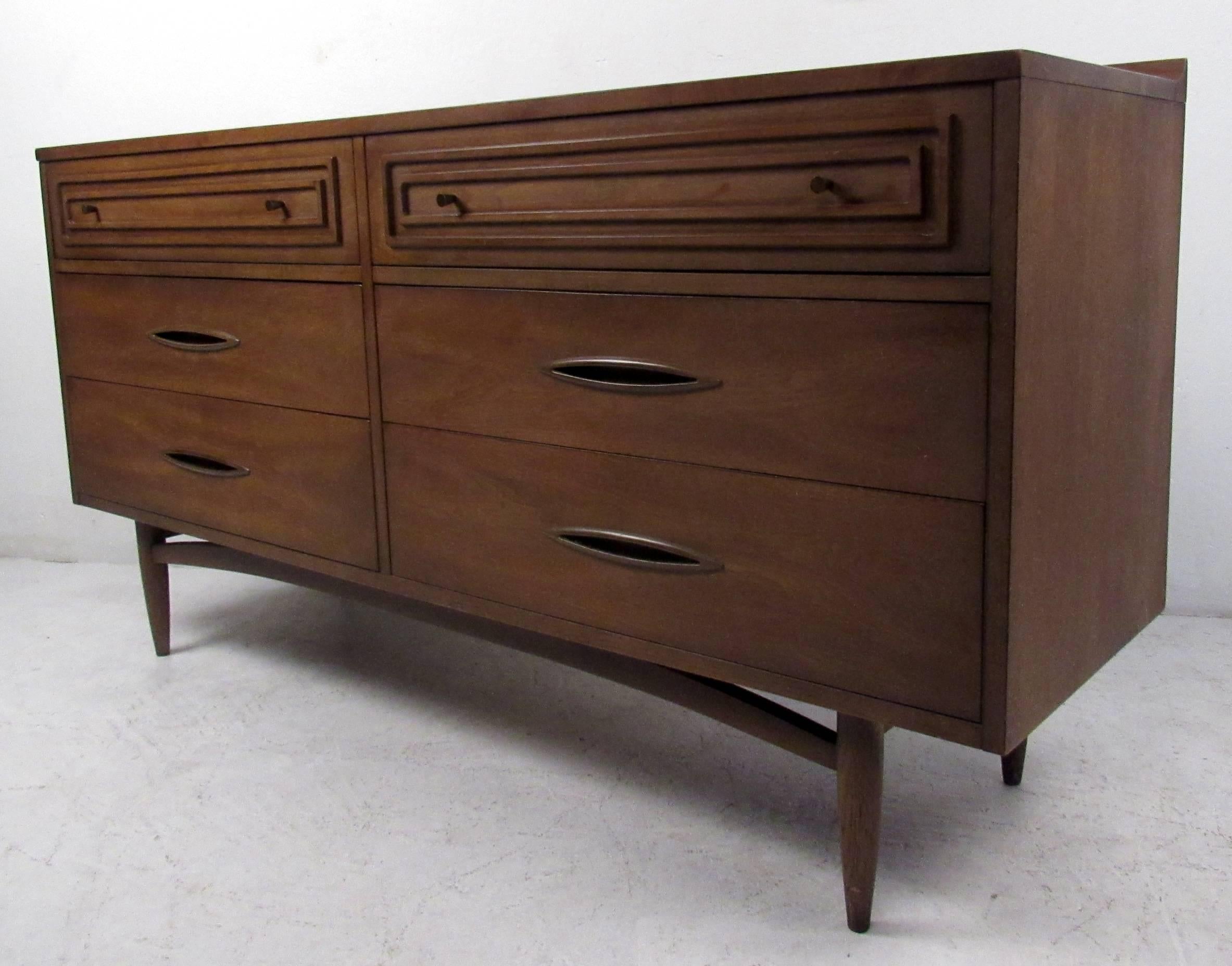 Vintage modern dresser featuring raised edge, six drawers and rich walnut grain throughout, manufactured by Broyhill. This well made case piece boasts oval recessed drawer pulls, a sculpted base, and tapered legs. A stylish mid-century dresser that