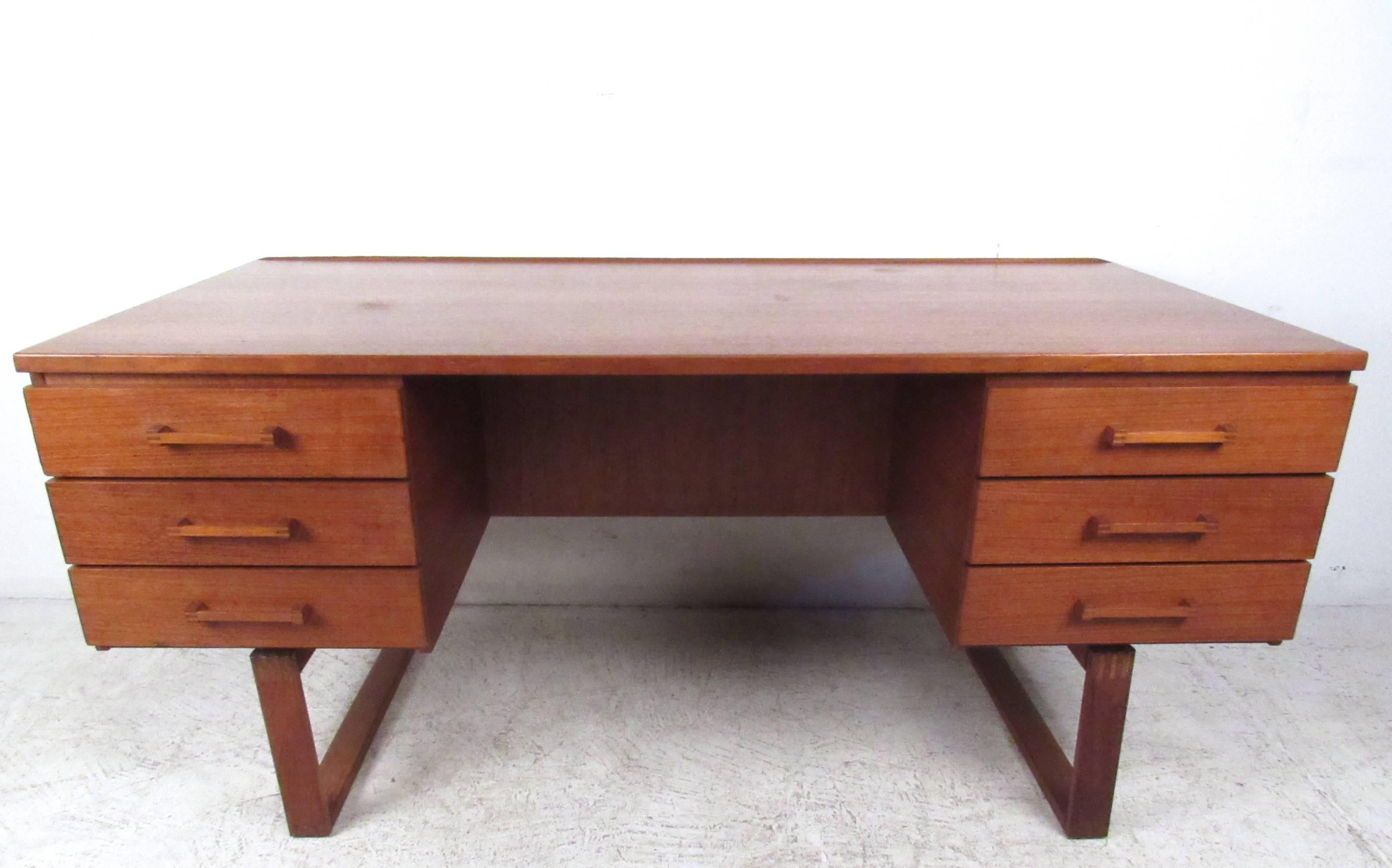 This beautiful vintage teak desk features unique sled leg construction, dovetail detail joints, and a raised edge top. Double-sided design offers a large open shelf on the backside of this six drawer workspace. Please confirm item location (NY or