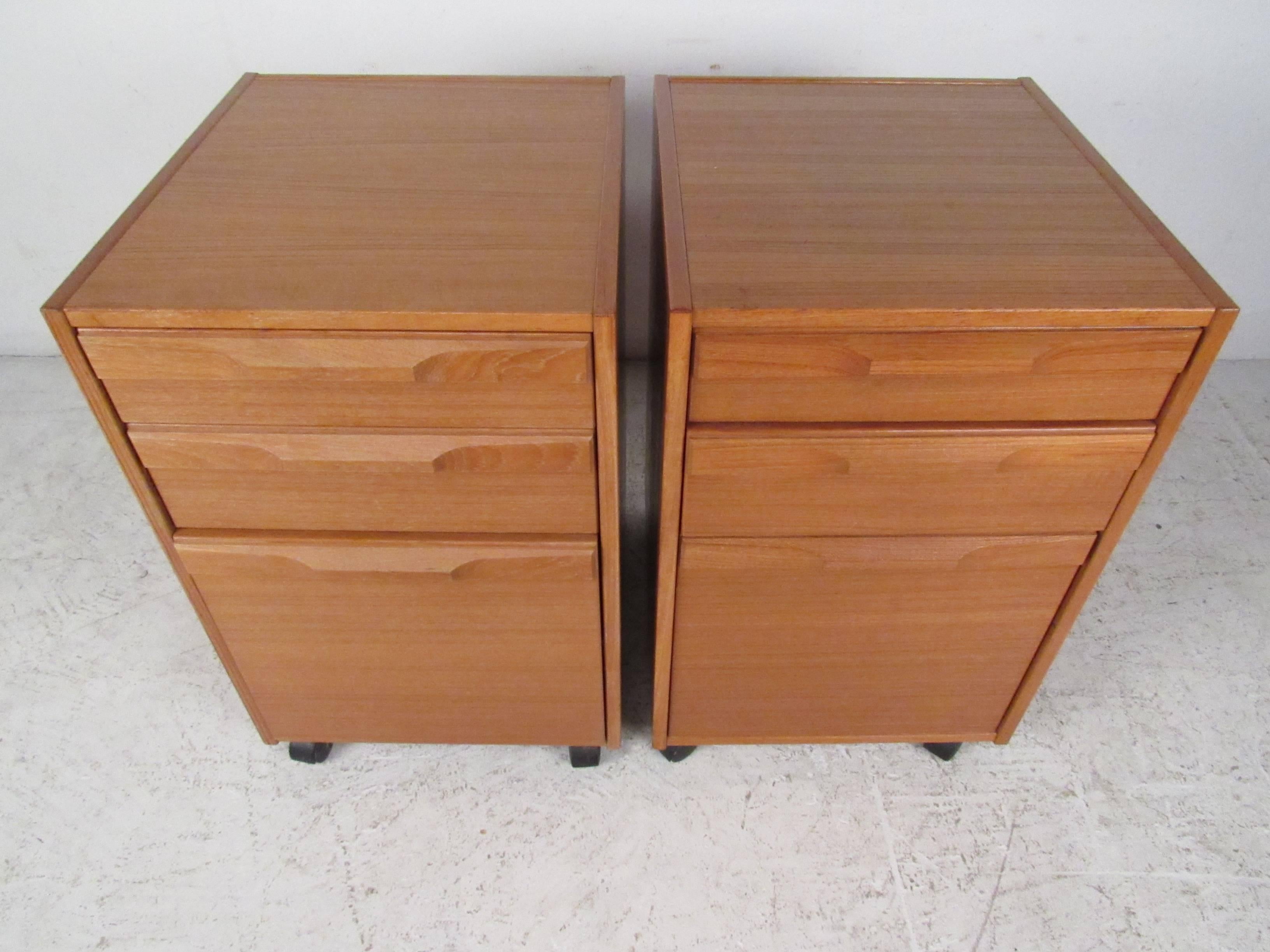 This pair of three drawer teak finish filing cabinets feature carved drawer handles, casters for easy mobility and unique Mid-Century design. Manufactured in Denmark by Denka, please confirm item location (NY or NJ).