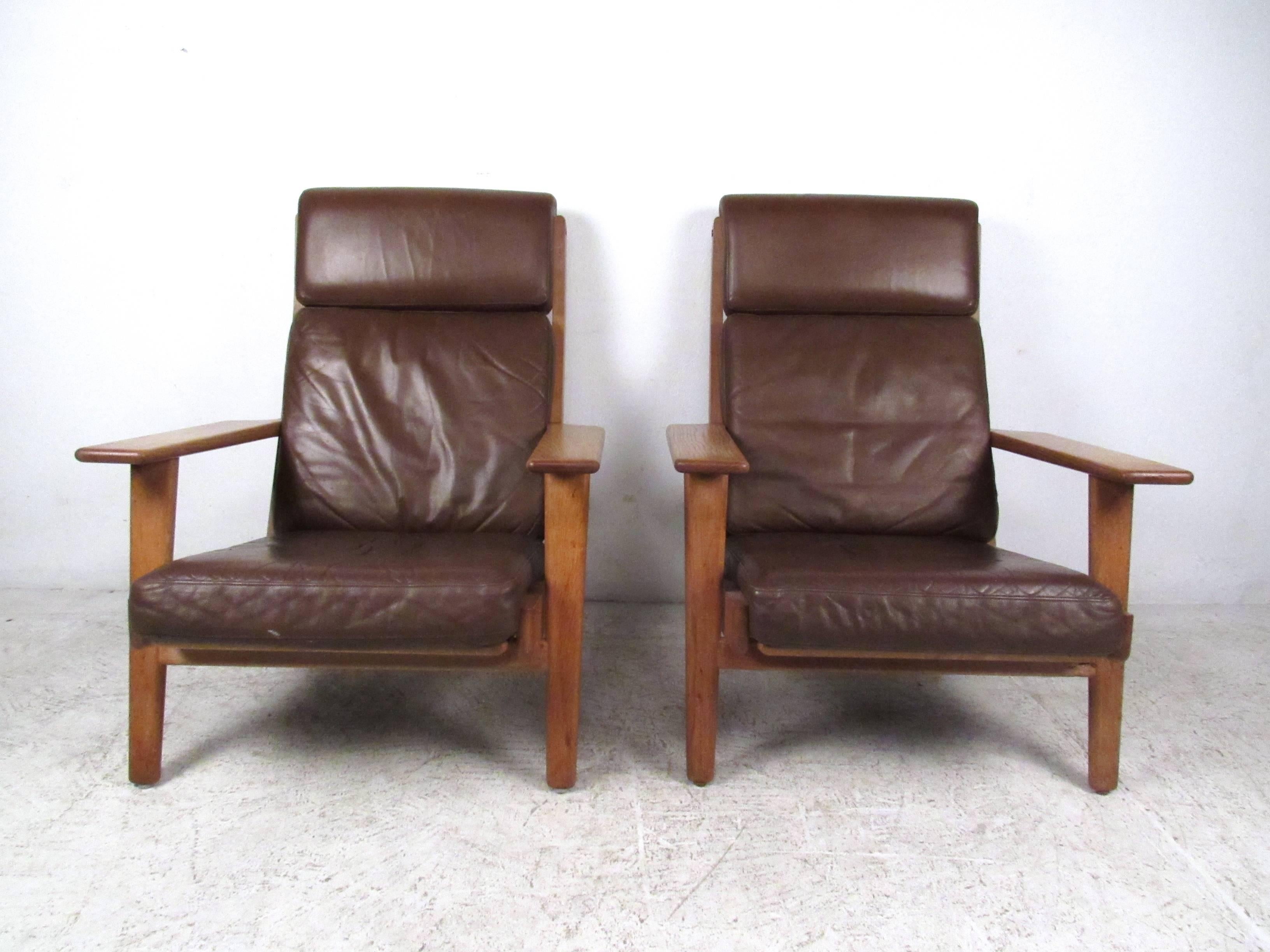 This beautiful vintage pair of brown leather lounge chairs feature the unique Mid-Century style of Hans Wegner. Slat backs, wide hardwood armrests and serpentine spring seats make this stylish pair of Getama GE-290 chairs a wonderful mix of comfort
