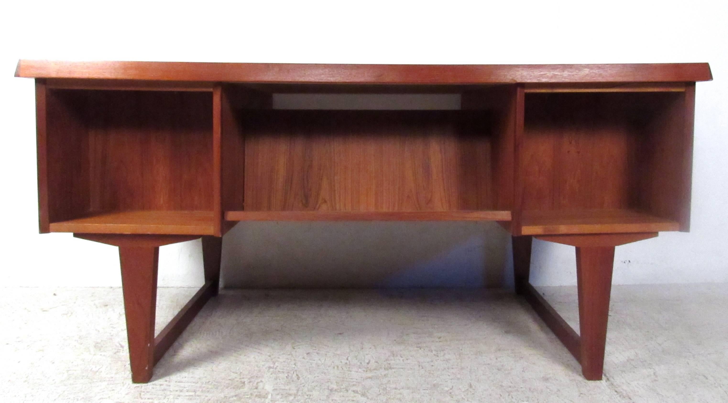 This stunning mid-century desk offers a unique workspace for home or office. The stylish tapered sled leg design is highly sought after, while the added shelves on the rear of the desk offers storage or display space. Carved drawer pulls and vintage