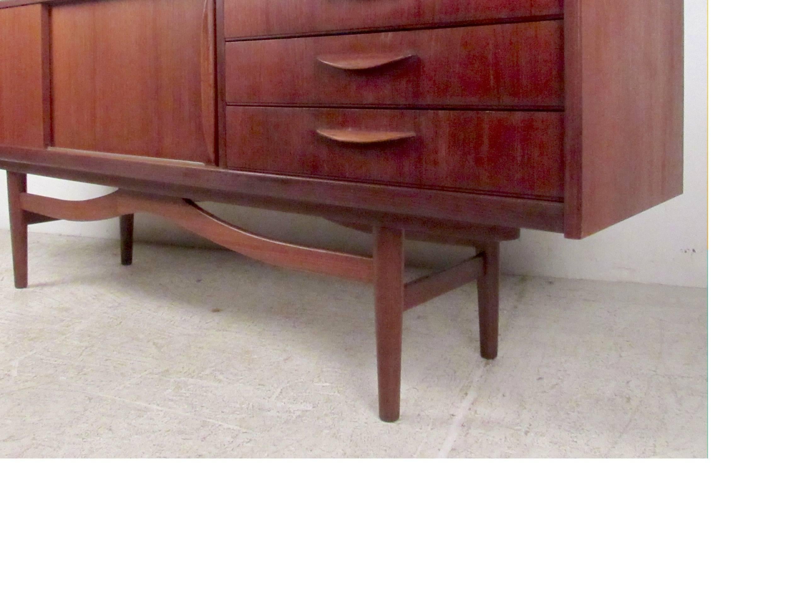 Vintage-modern Danish sideboard featuring beautifully sculpted base and handles with rich teak wood grain throughout.

Please confirm item location NY or NJ with dealer.