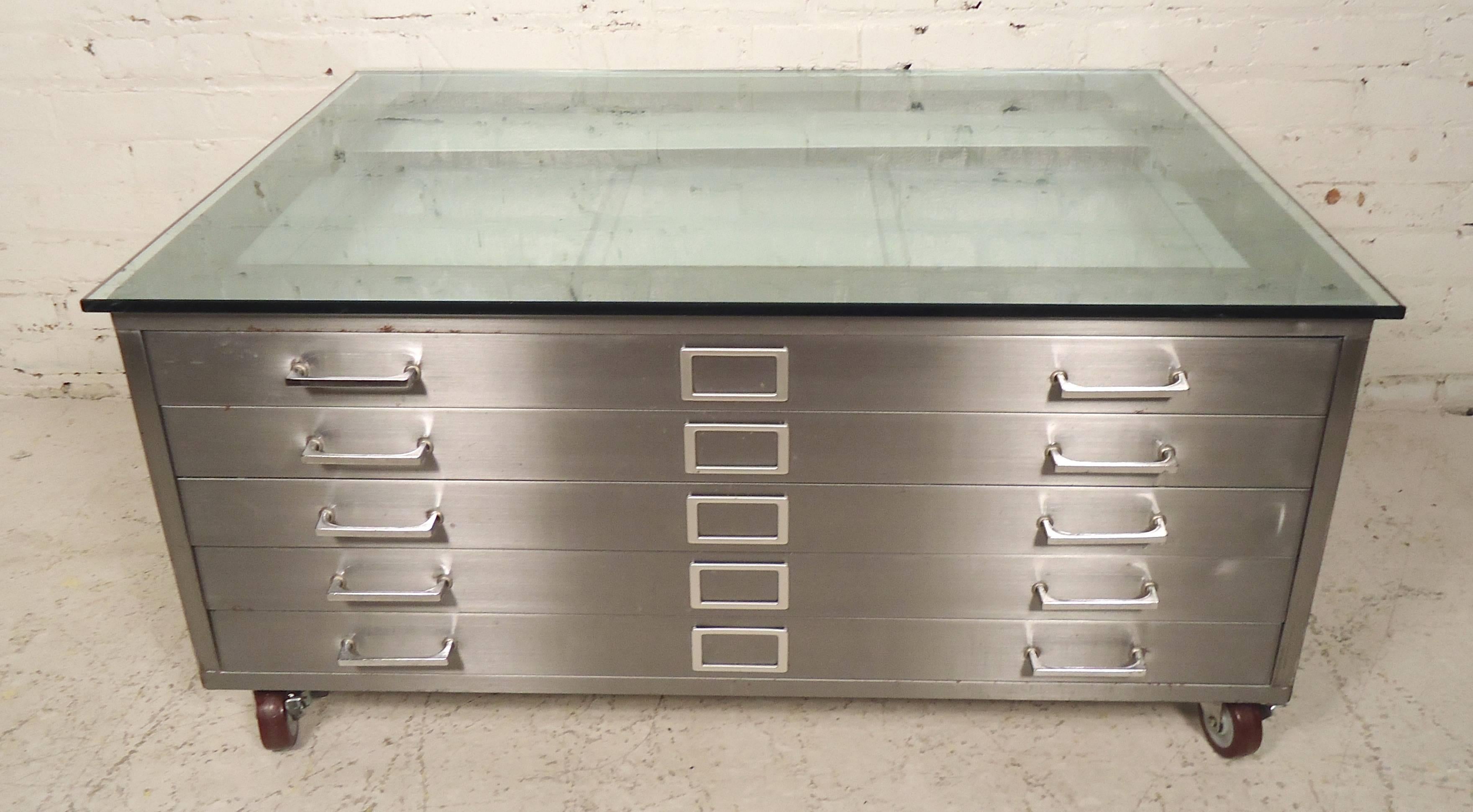 Unique stainless steel coffee table with glass top. Re-purposed architects flat file cabinet, made into a modern coffee table with braking wheels.

 (Please confirm item location - NY or NJ - with dealer).
 