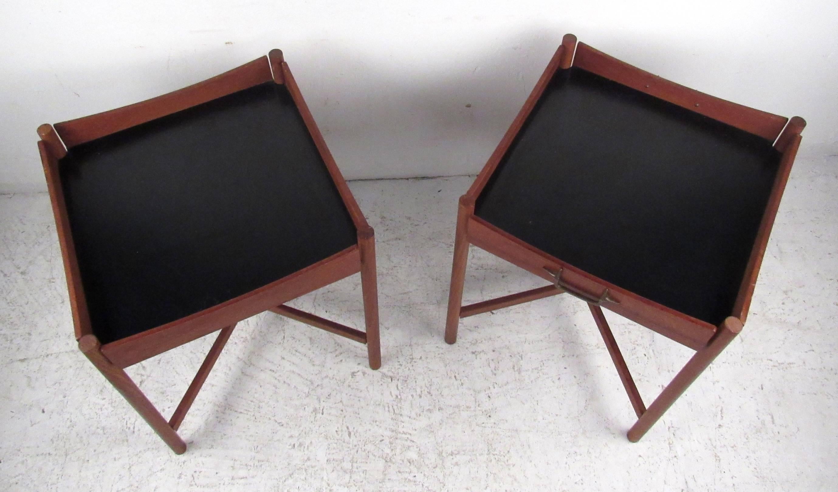 Two vintage modern tray tables featuring sculpted teak frames, black formica tops and brass handles. Designed by mid-century artist Mogens Lysell, these tray tables are as handy as they are distinct. Perfect for holding indoor plants, or concealing
