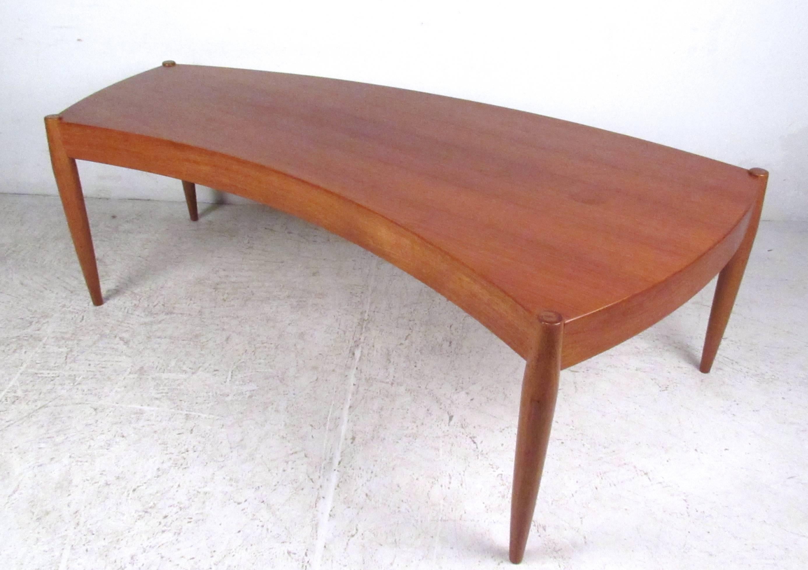 This beautiful vintage coffee table features a wonderful sculpted edge construction paired with tall tapered legs. Beautiful wood tone and unique shape makes this the perfect partner to the matching sofa and lounge chairs we also have available.