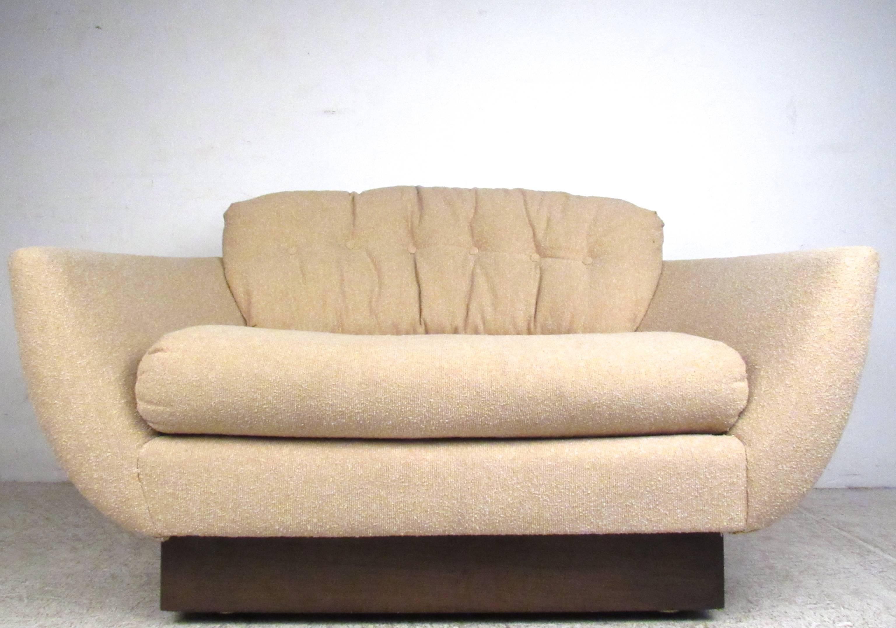 This loveseat style lounge chair features a wide sculpted seat with comfortable upholstery and tufted cushion. Wood trim base adds charm to it's Mid-Century style, please confirm item location (NY or NJ).