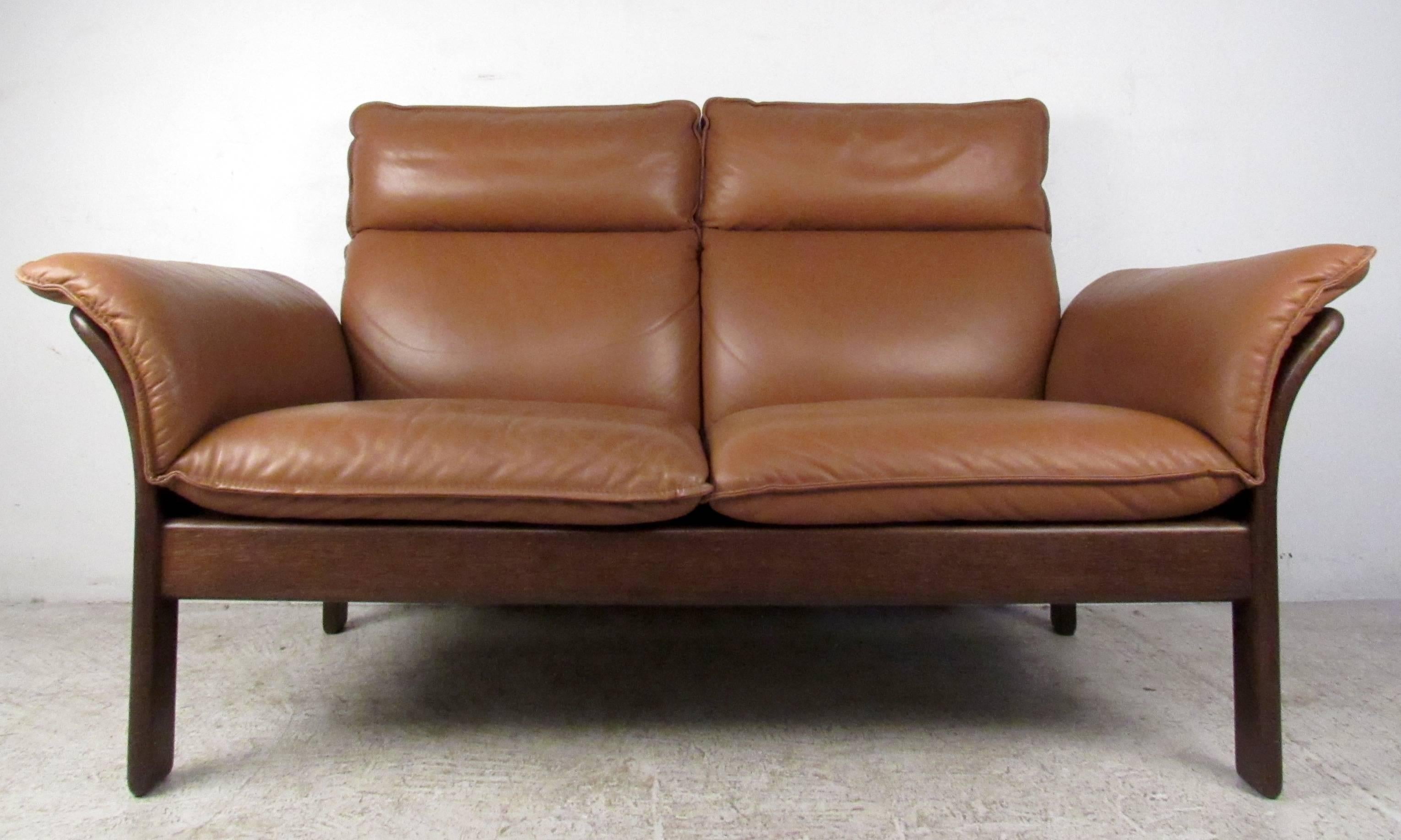 Vintage-modern loveseat featuring sculpted rosewood frame and orange leather upholstery. A sleek design with winged arm rests and beautiful rosewood grain throughout. This stylish and comfortable sofa makes the perfect addition to any home,