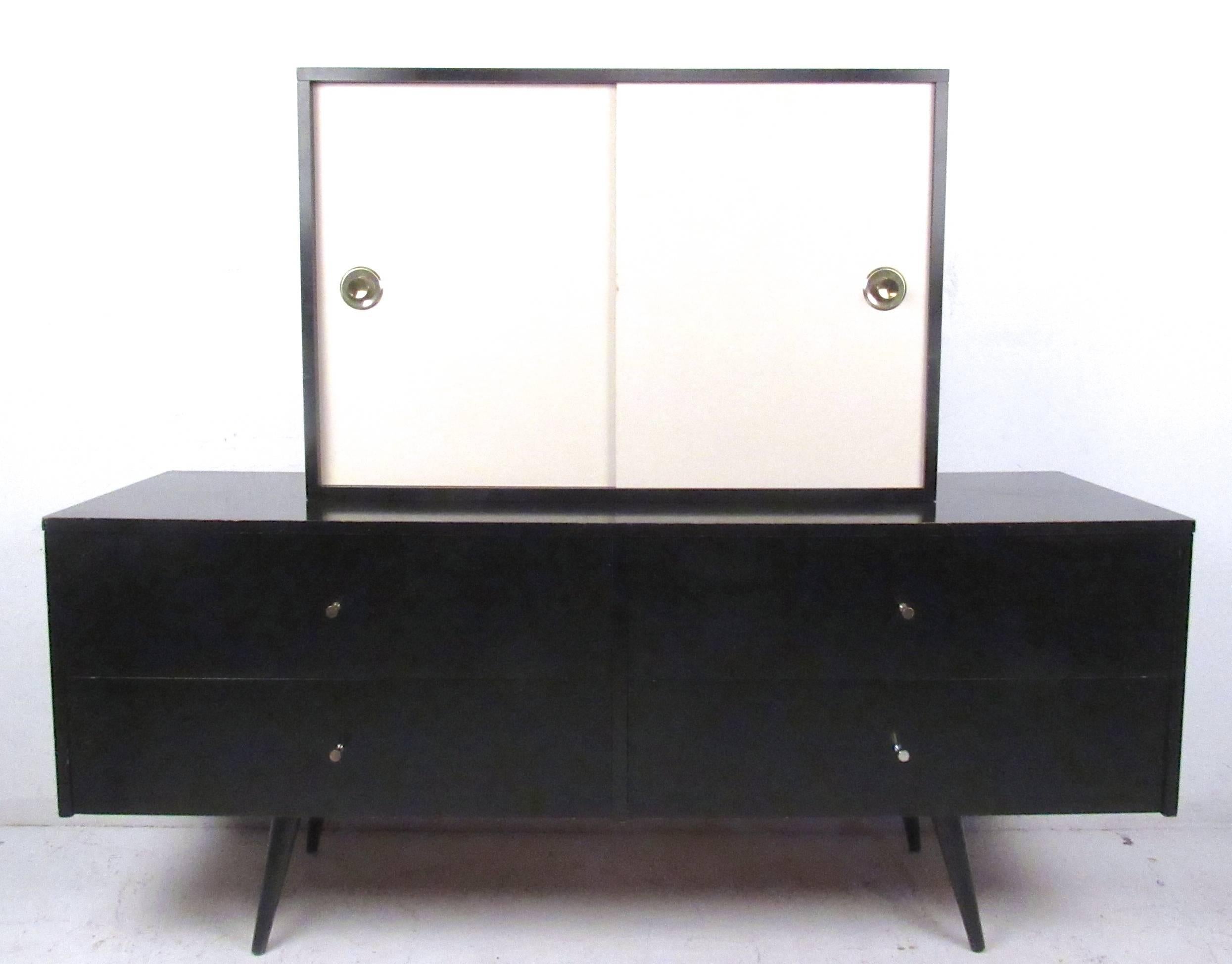 This unique two-piece credenza by Paul McCobb features four drawers for storage and a sliding door cabinet topper. Classic Paul McCobb design is evident with unique pulls, tapered legs, and clean lines (original label intact). Please confirm item