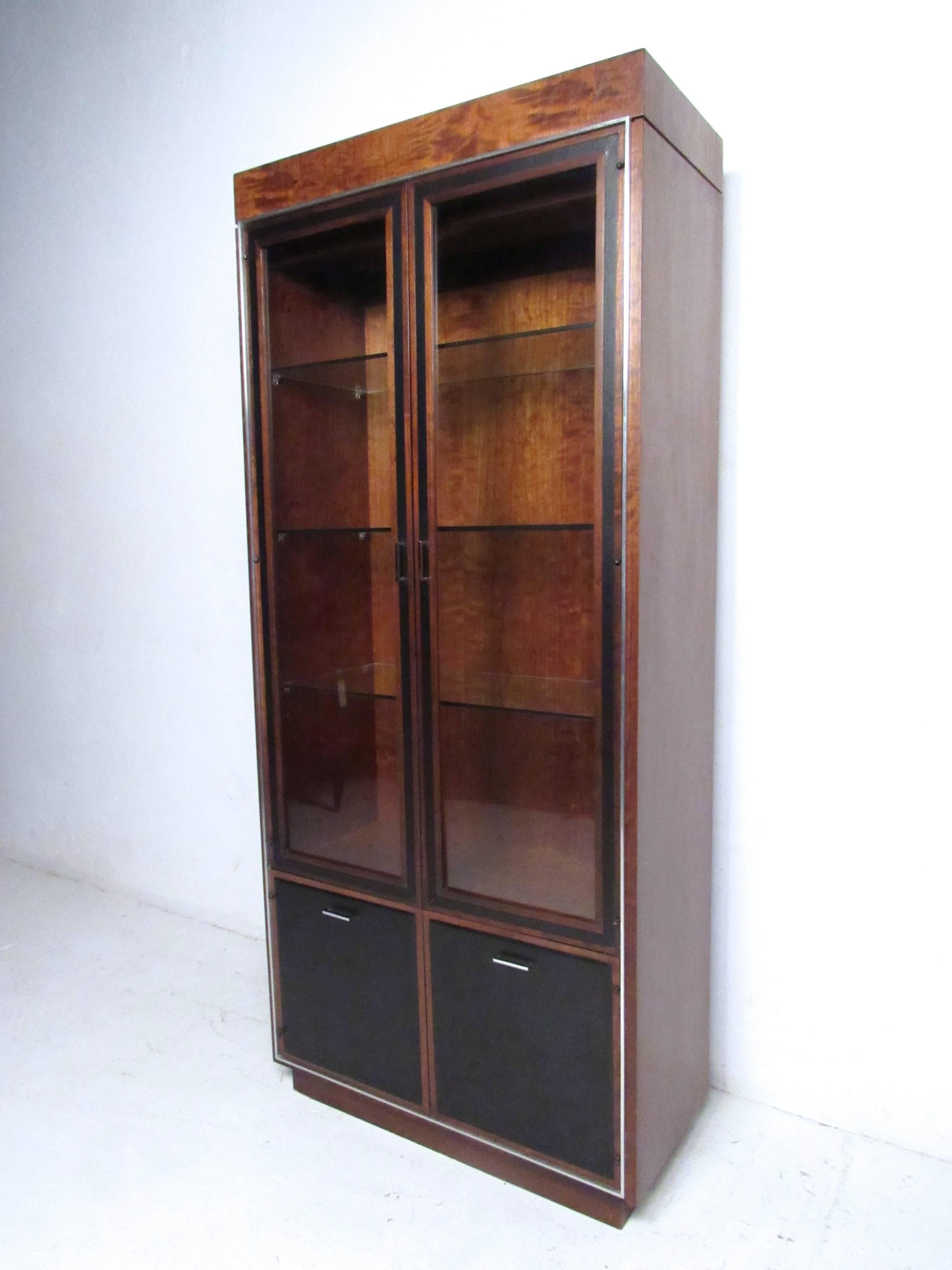 This beautiful Mid-Century display cabinet offers spacious storage behind oversized glass doors, with a lower shelved cabinet enclosed with leather front doors. Unique chrome trim, stylish John Stuart pulls and top light option make this piece a