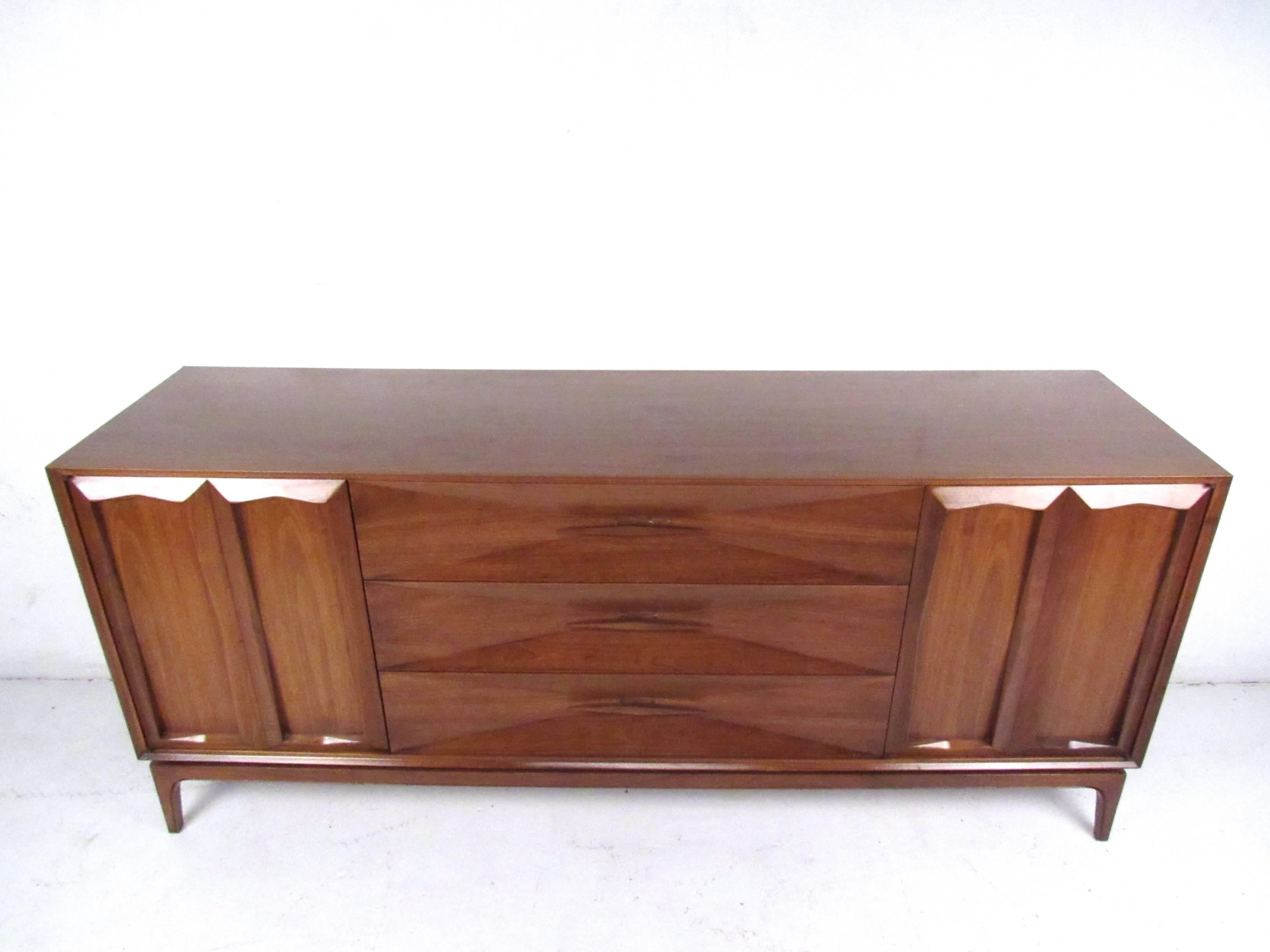 This beautiful vintage nine-drawer dresser features beautiful sculpted drawer fronts and makes a lovely Mid-Century addition to any room. Wonderful natural wood finish, unique drawer pulls and tapered legs showcase the craftsmanship and beauty of