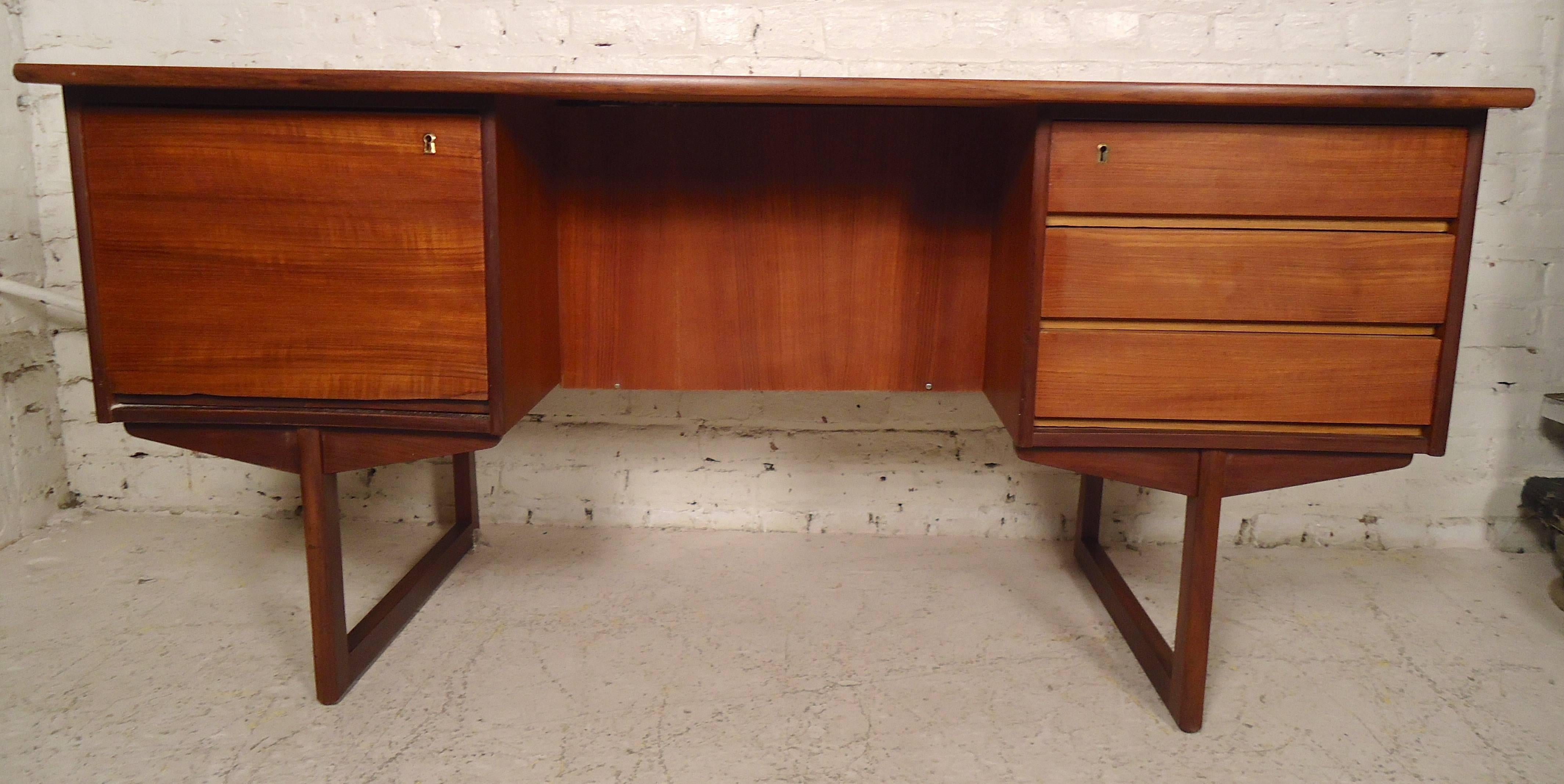 Danish desk with finished back and sled legs with warm teak grain. Three drawers with sculpted pulls, back storage and long desk top. Impressive double-sided design offers additional shelf storage/display along with the spacious filing cabinet and