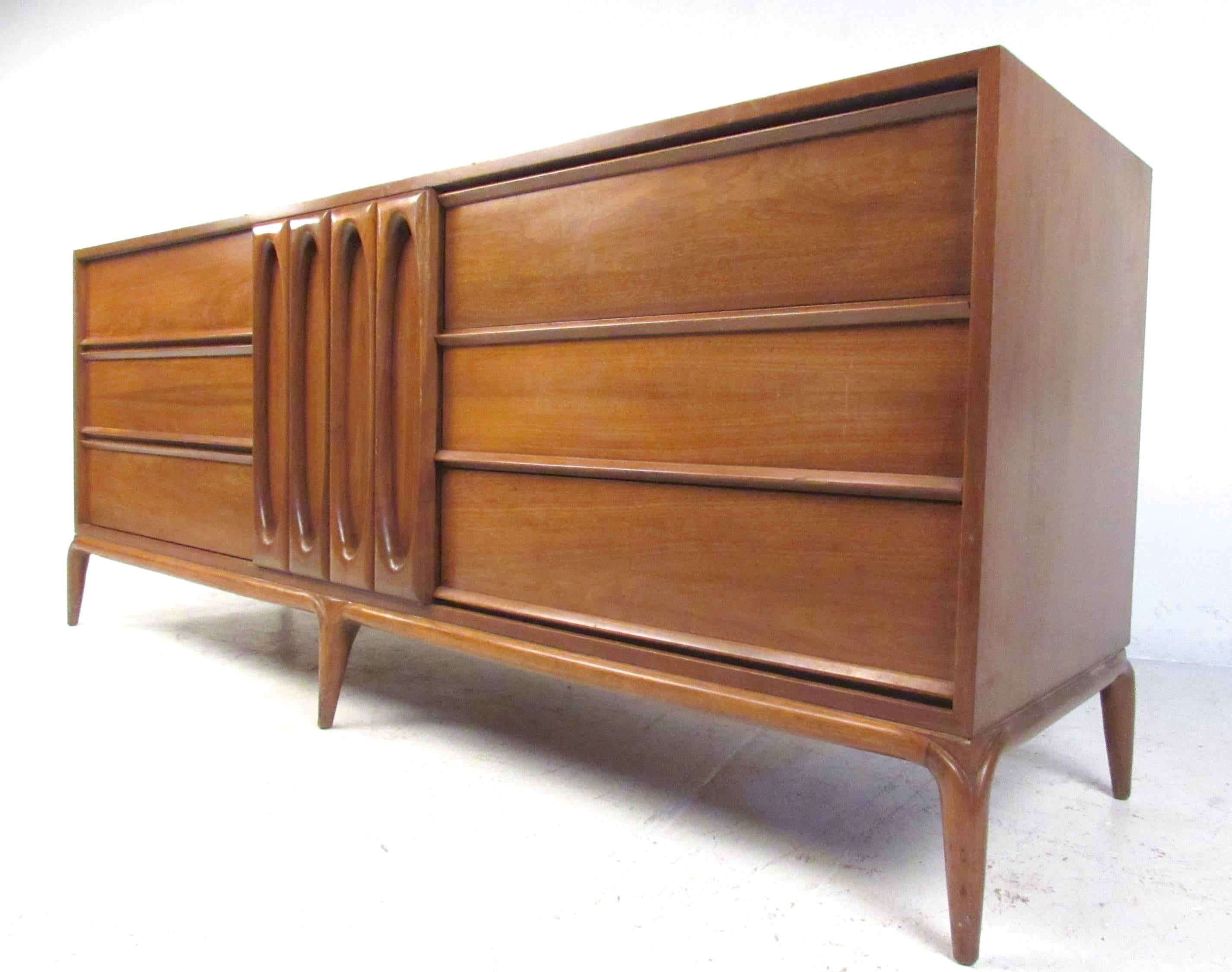 Beautiful vintage walnut finish is accented by decorative cabinet front that conceals three smaller drawers. Straight lines, sculpted door fronts, and splayed legs show attention to detail on this stylish case piece. This Mid-Century American