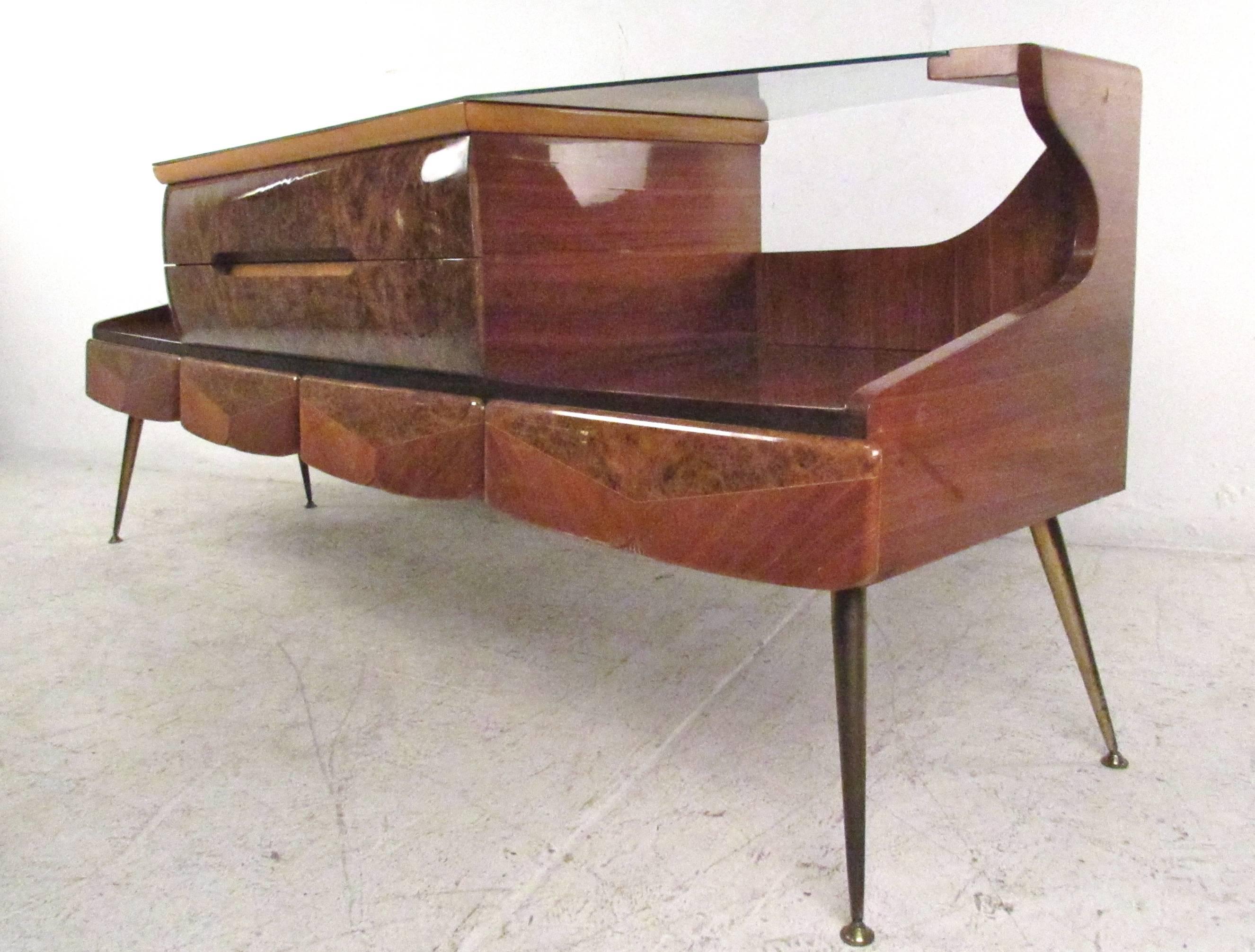 This stunning vintage sideboard features a lacquered burl wood finish, tapered brass legs, textured glass top and a unique shape. Please confirm item location (NY or NJ.)