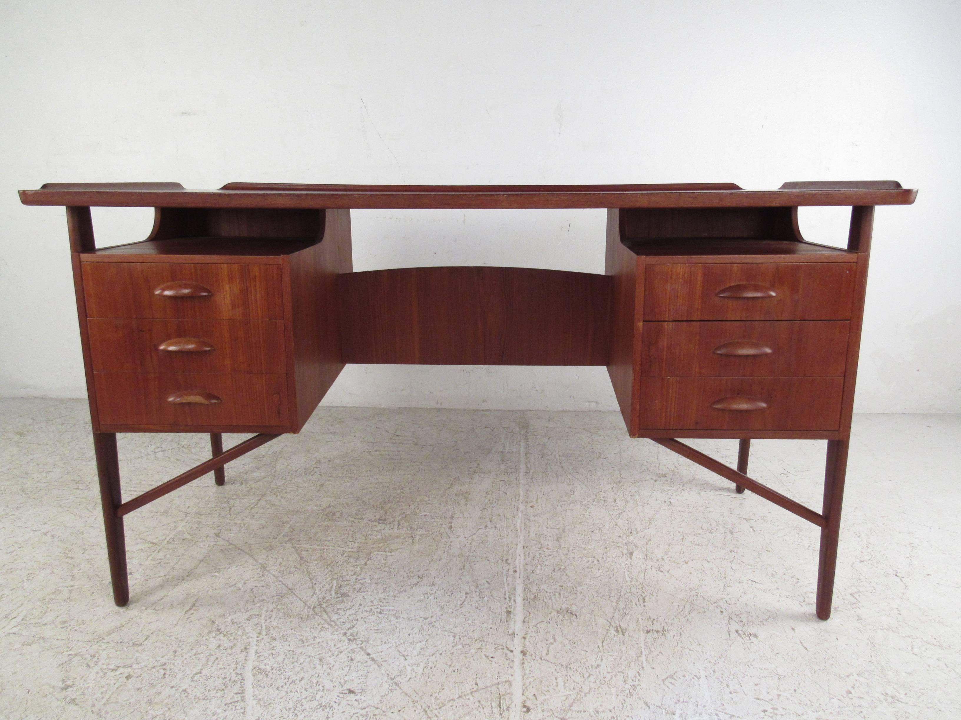 This double-sided teak desk features wonderful Mid-Century design, with raised edges, curved handles, and drop front cabinet storage on the rear side. Mirrored bar, and display shelf round out the vintage charm of the desk, making it a stylish