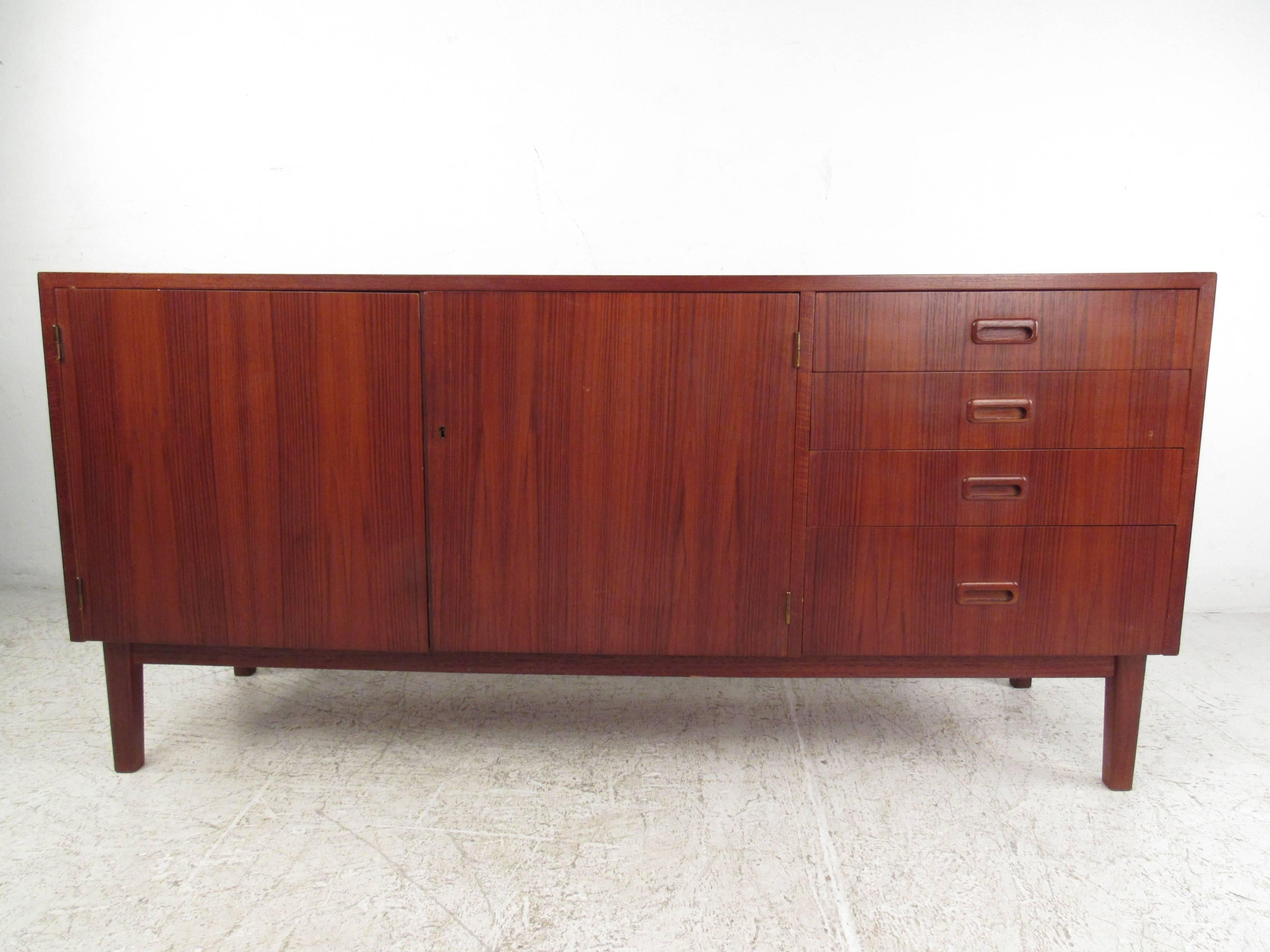 This vintage credenza features a unique reddish teak finish, with dual door cabinet storage, four carved pull drawers, and a miniature foot print perfect for tight spacing. Excellent Mid-Century piece for use as a television stand, service cabinet,