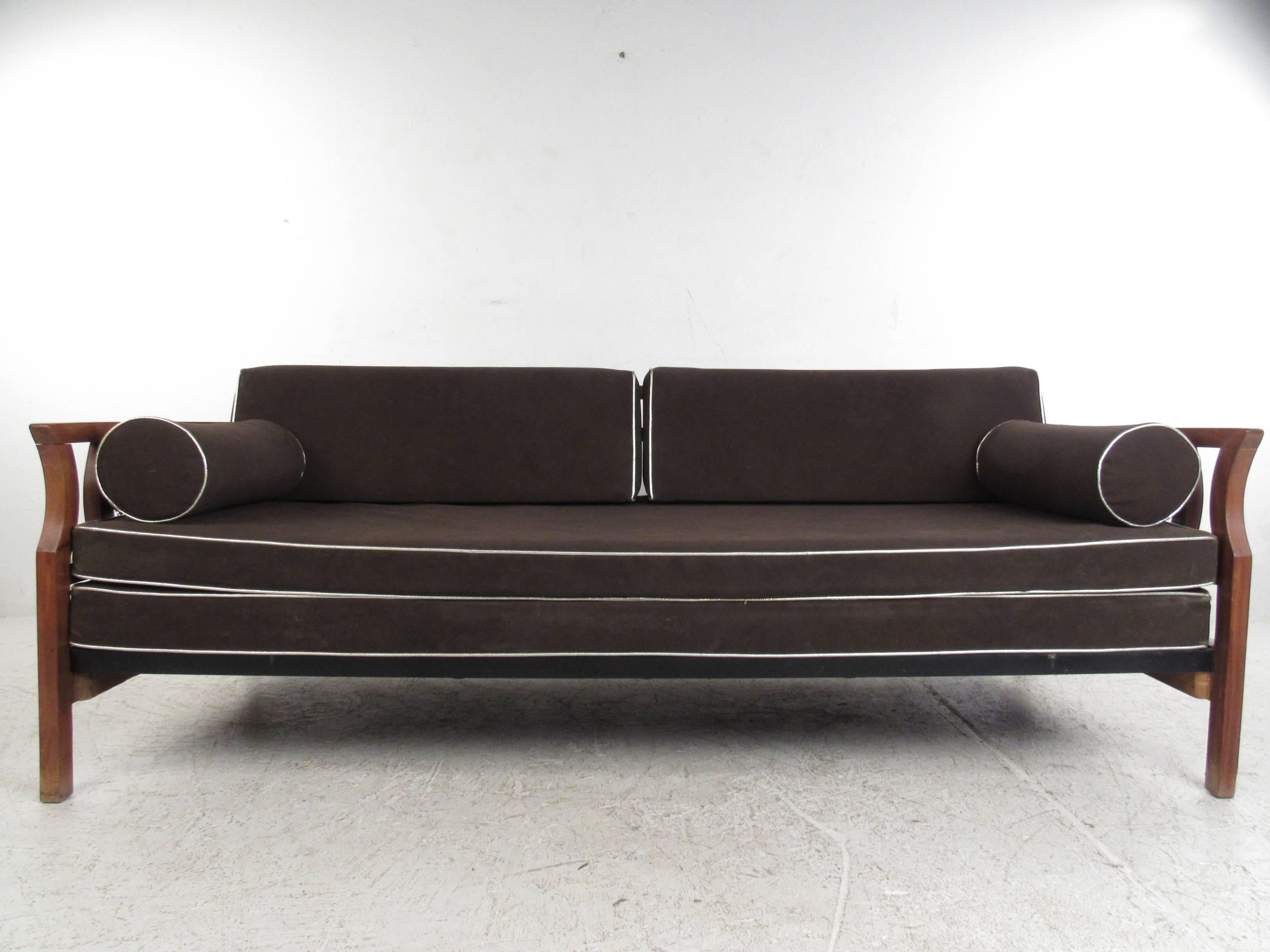 This unique double cushion sofa features sturdy construction and unique 1960s design. Sculptural walnut frame features double oval cutaway arms, with a sturdy iron spring bottom. Angled seat back and cylindrical pillows add to it's vintage charm.